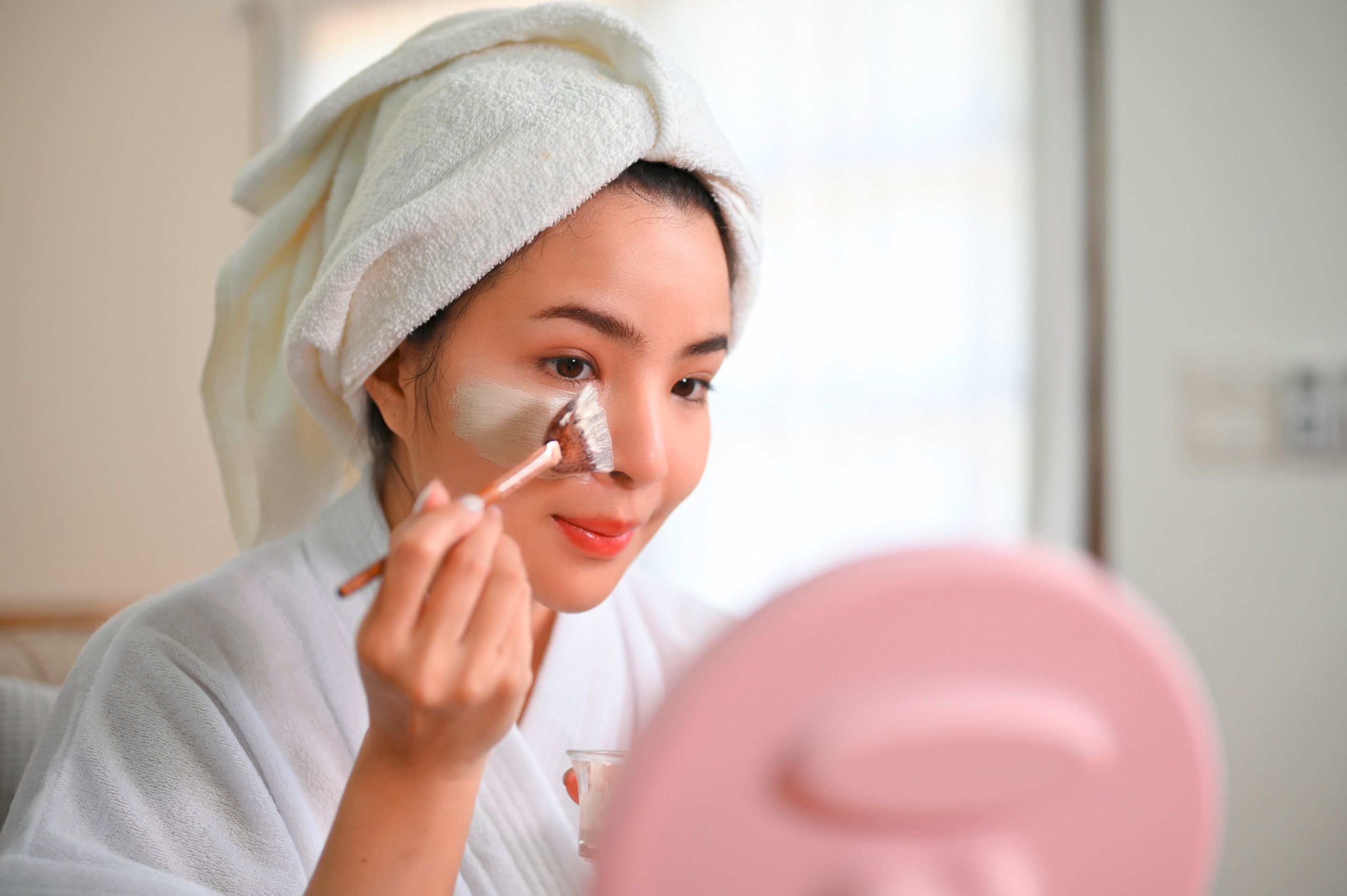 Woman applying clay mask to her face with a flat brush.