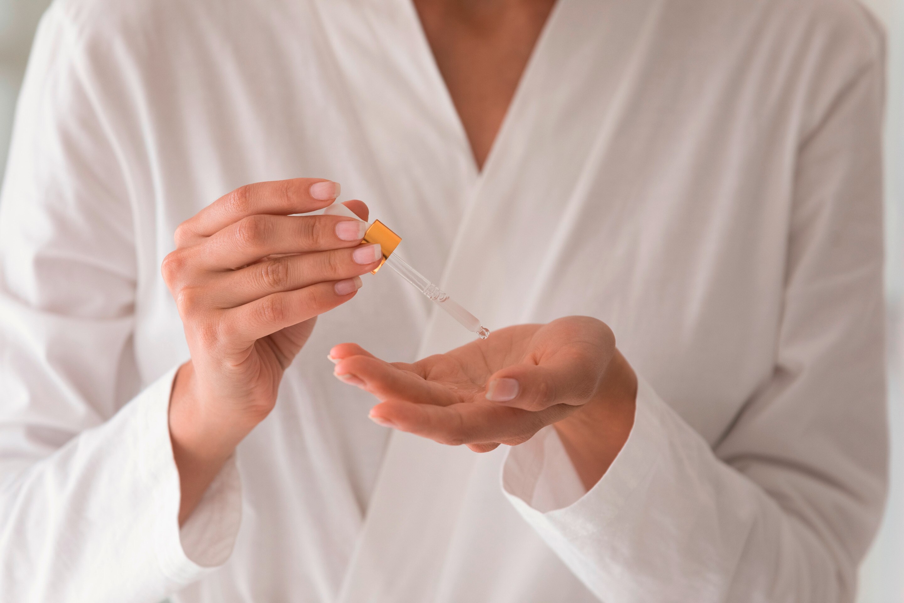 A woman dispensing serum from a dropper onto her hand.