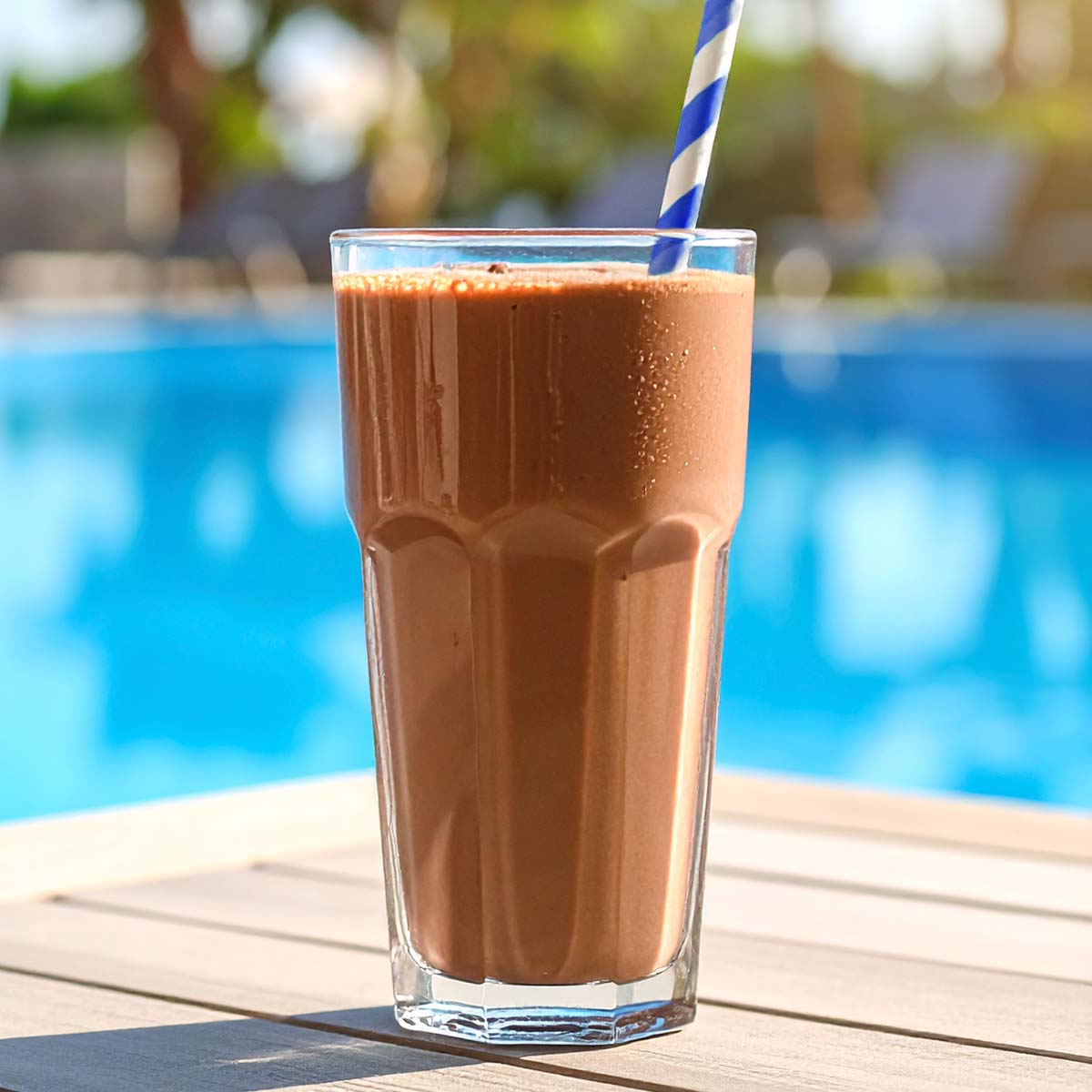 Glass of Frozen Peanut Butter Cocktail with a pool on the background 