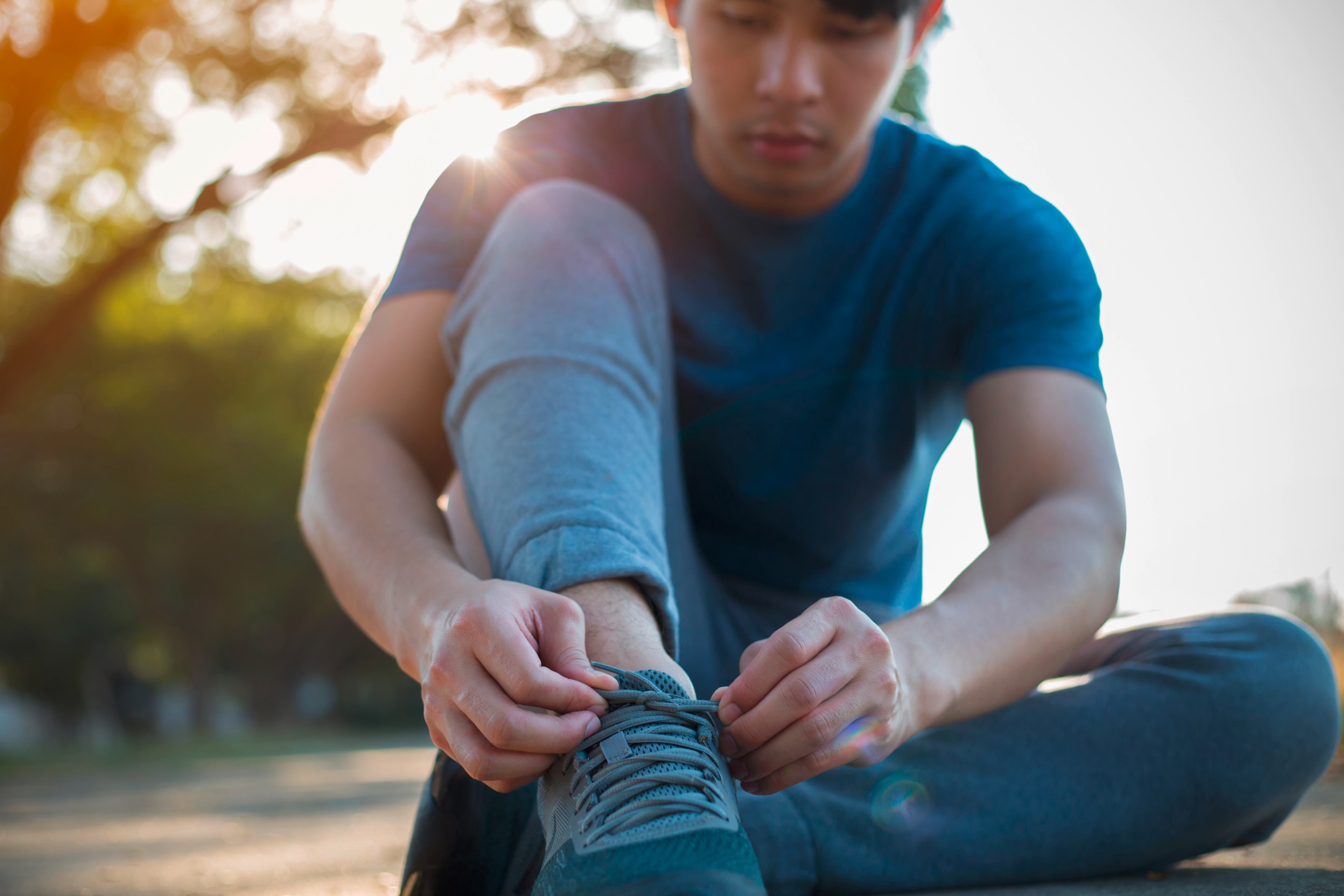 Asian man tying shoelaces outdoors.