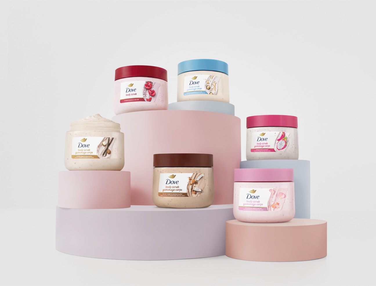 Dove Crushed Cherries & Chia Milk, Brown Sugar and Coconut Butter and Crushed Macadamia and Rice Milk Body Scrubs standing or laid against a white background. There are three jars without their lids on and the product's whipped texture is shown.