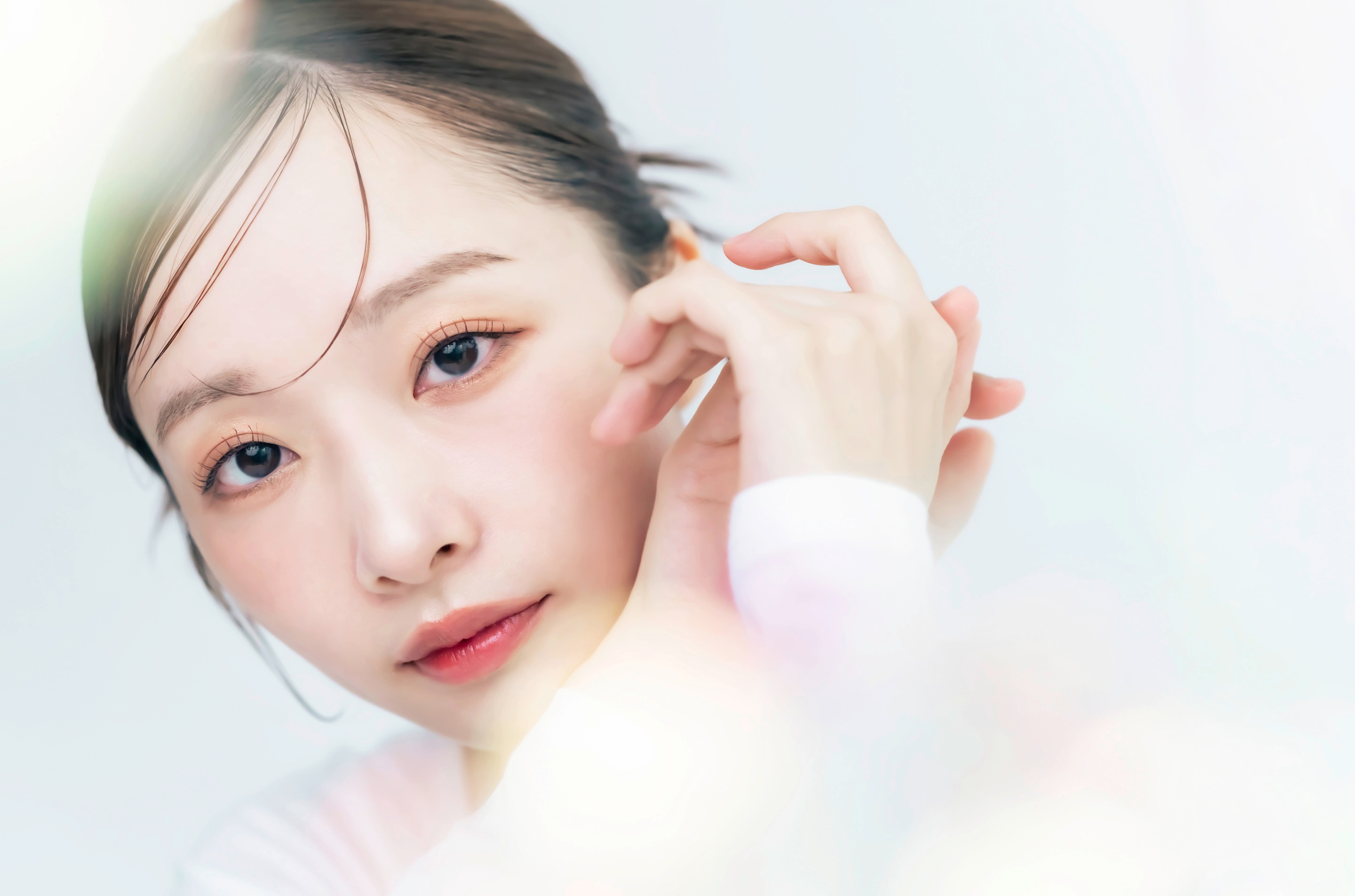ผู้หญิงเอเชีย เอียงหน้า ผิวสวย รวบผม มีลำแสงสีรุ้งฟุ้งกระจาย ใช้สองมือประกบ ยกขึ้นใกล้ใบหน้า