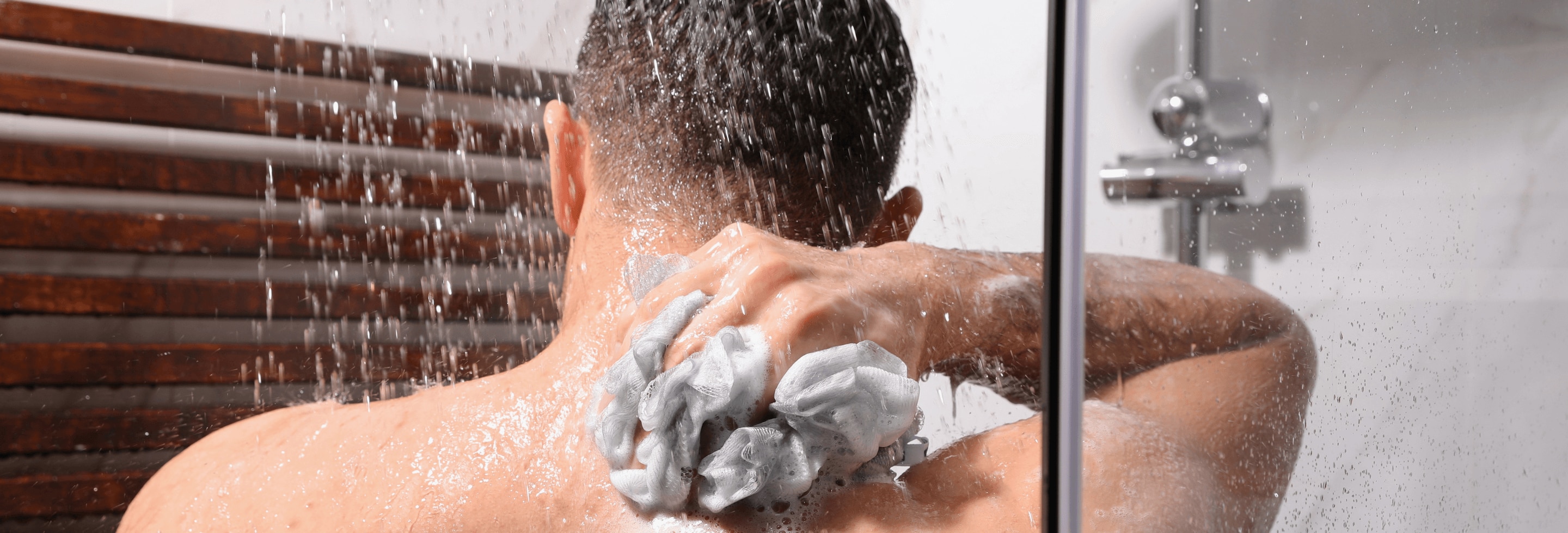 Man using a plastic loofah with body wash in the shower
