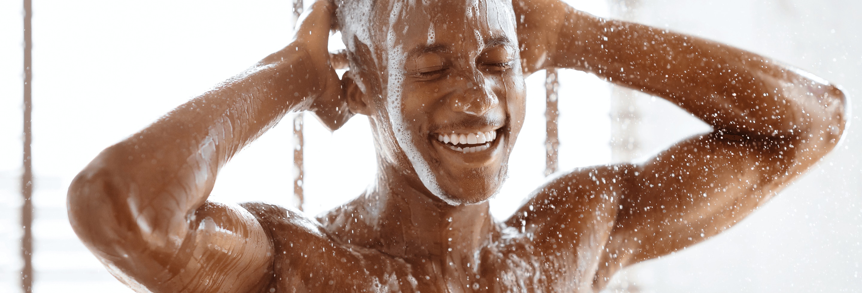 Young African American man washing his hair and body under a hot shower