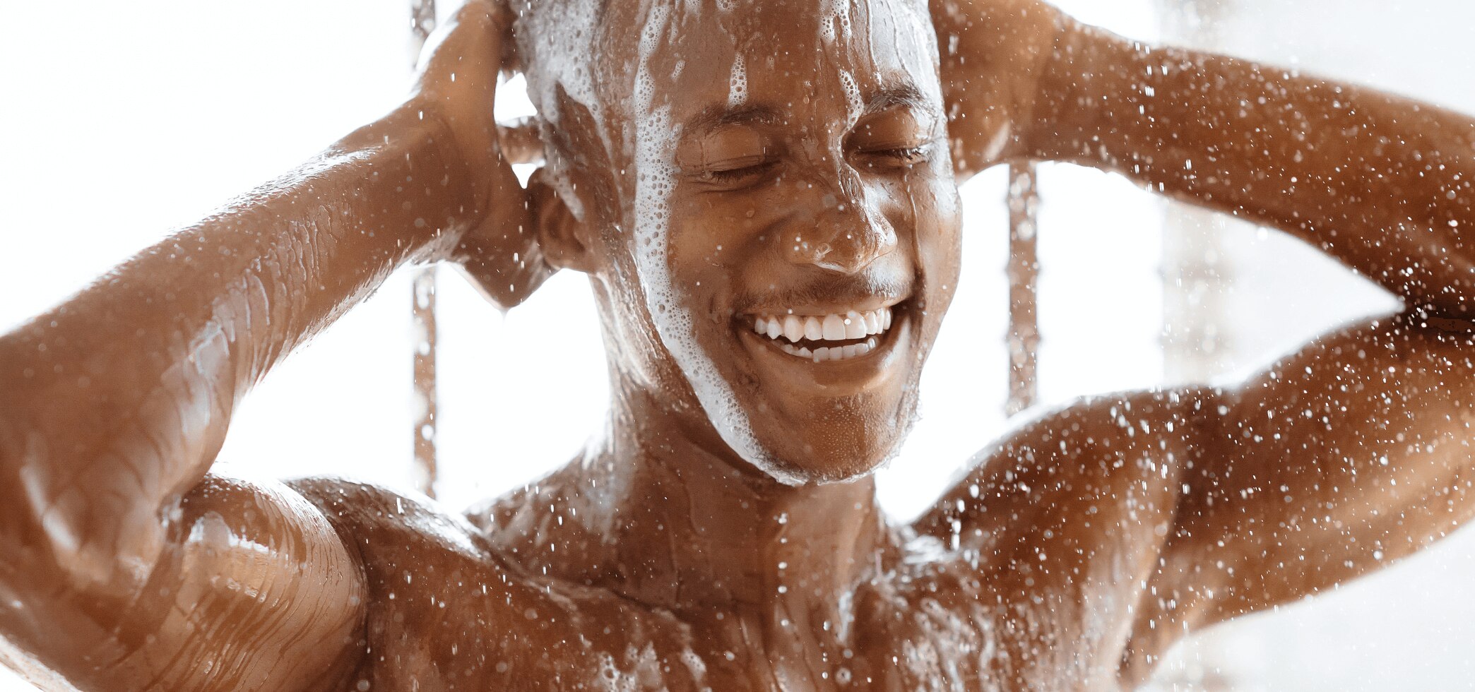 Young African American man washing his hair and body under a hot shower