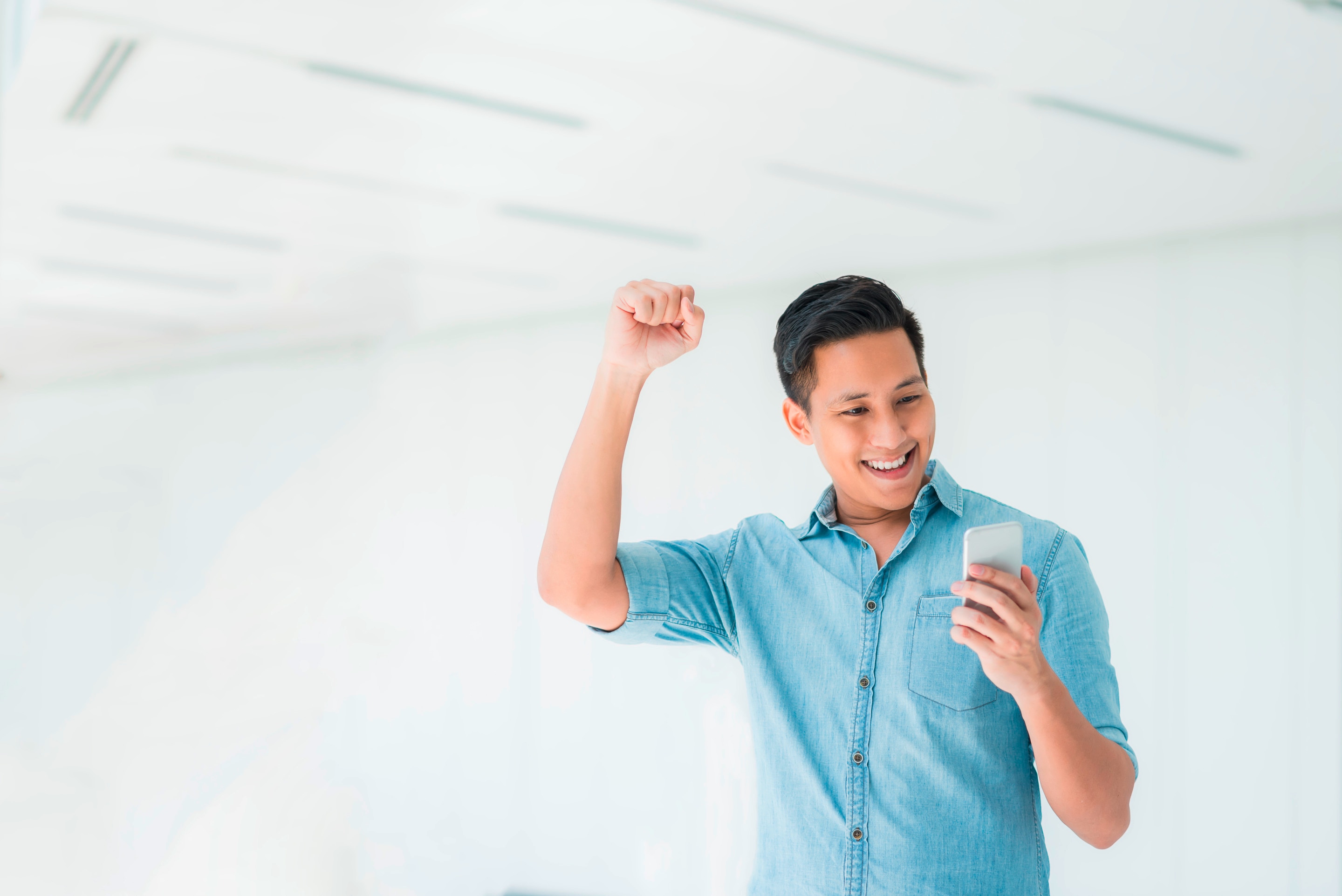 Asian man looking at phone and raising his arm.