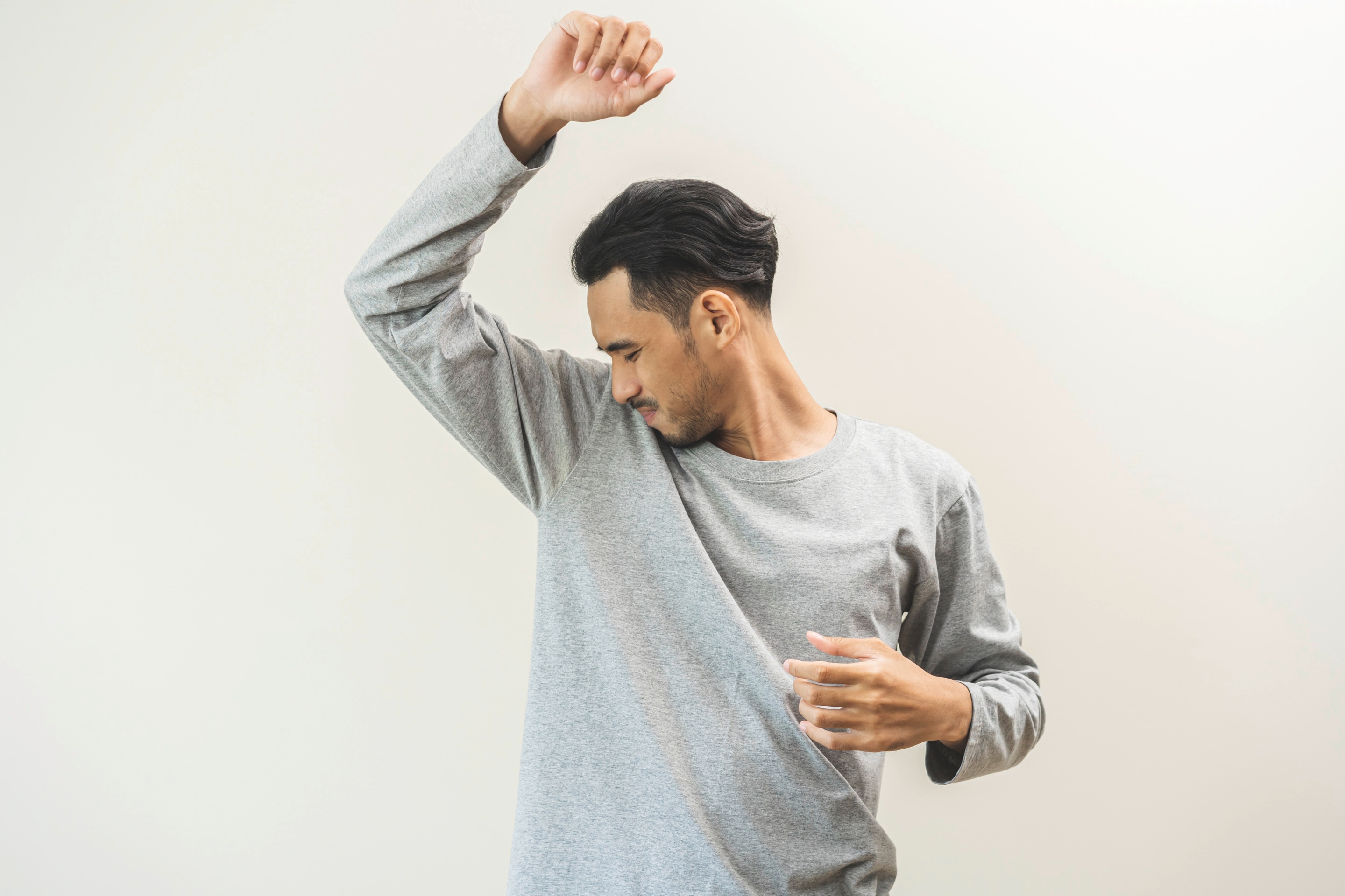 Asian man in gray shirt smelling his underarm.