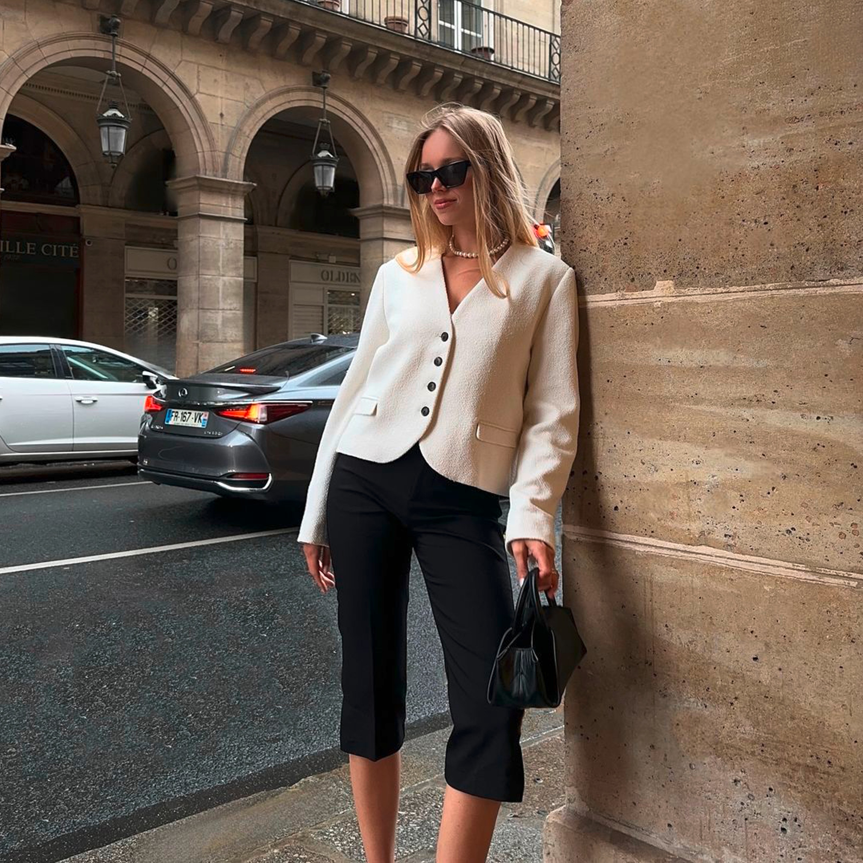 A portrait of woman wearing beige checkered capri pants, white vest top, and blue cardigan.