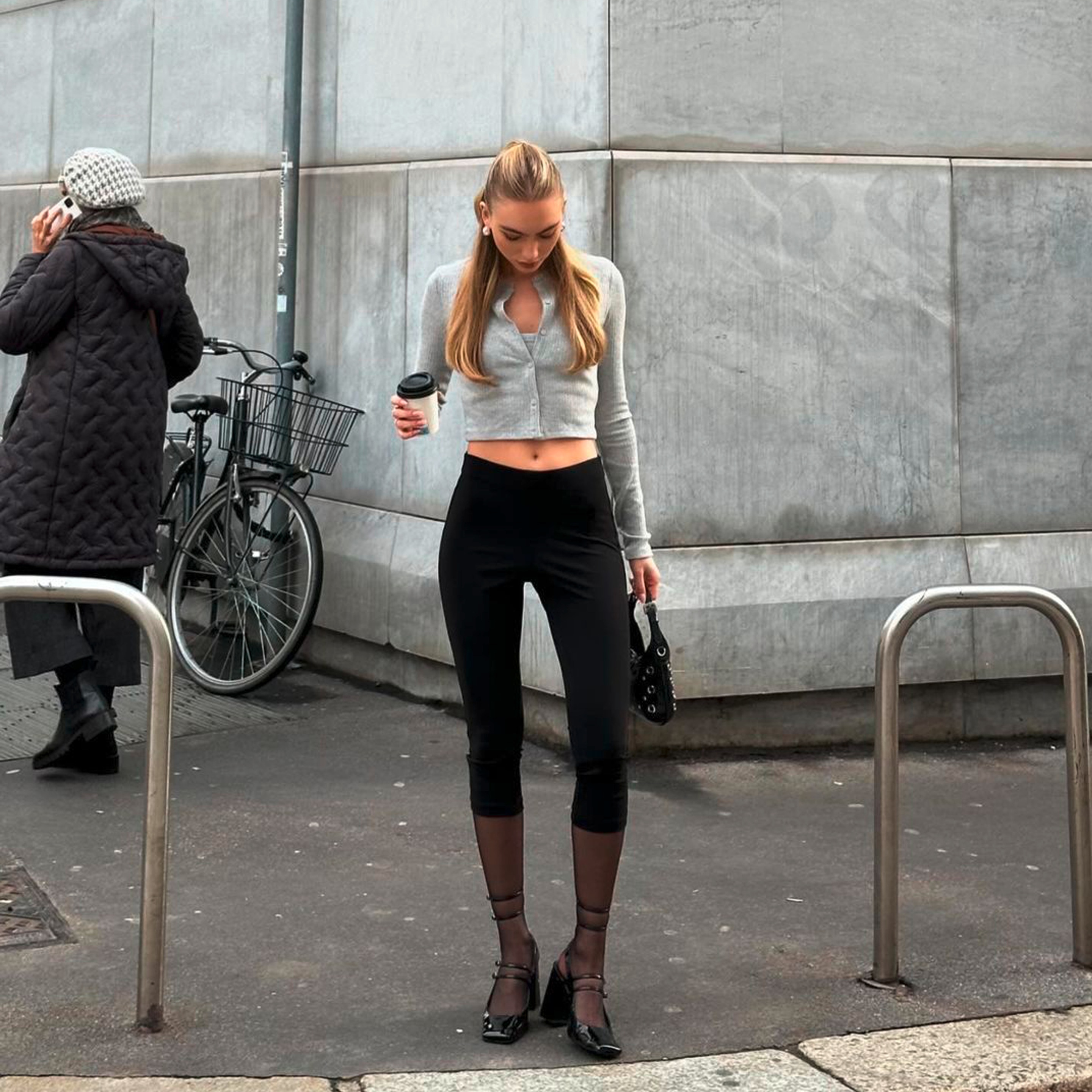 A portrait of woman wearing beige checkered capri pants, white vest top, and blue cardigan.