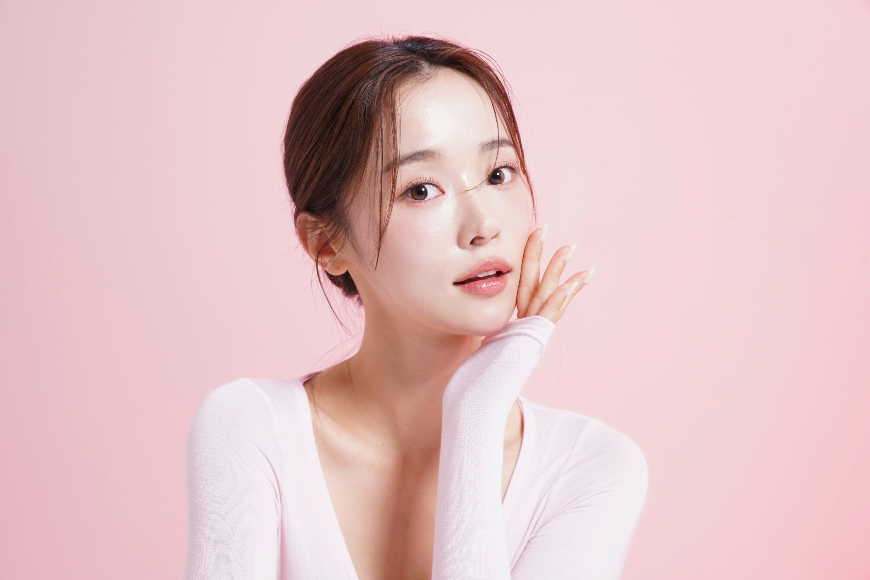 ผู้หญิงเอเชีย ผิวสวย รวบผม เอานิ้วขึ้นมาแตะบนใบหน้าที่เอียงเล็กน้อย สวมเสื้อแขนยาวแนบเนื้อ