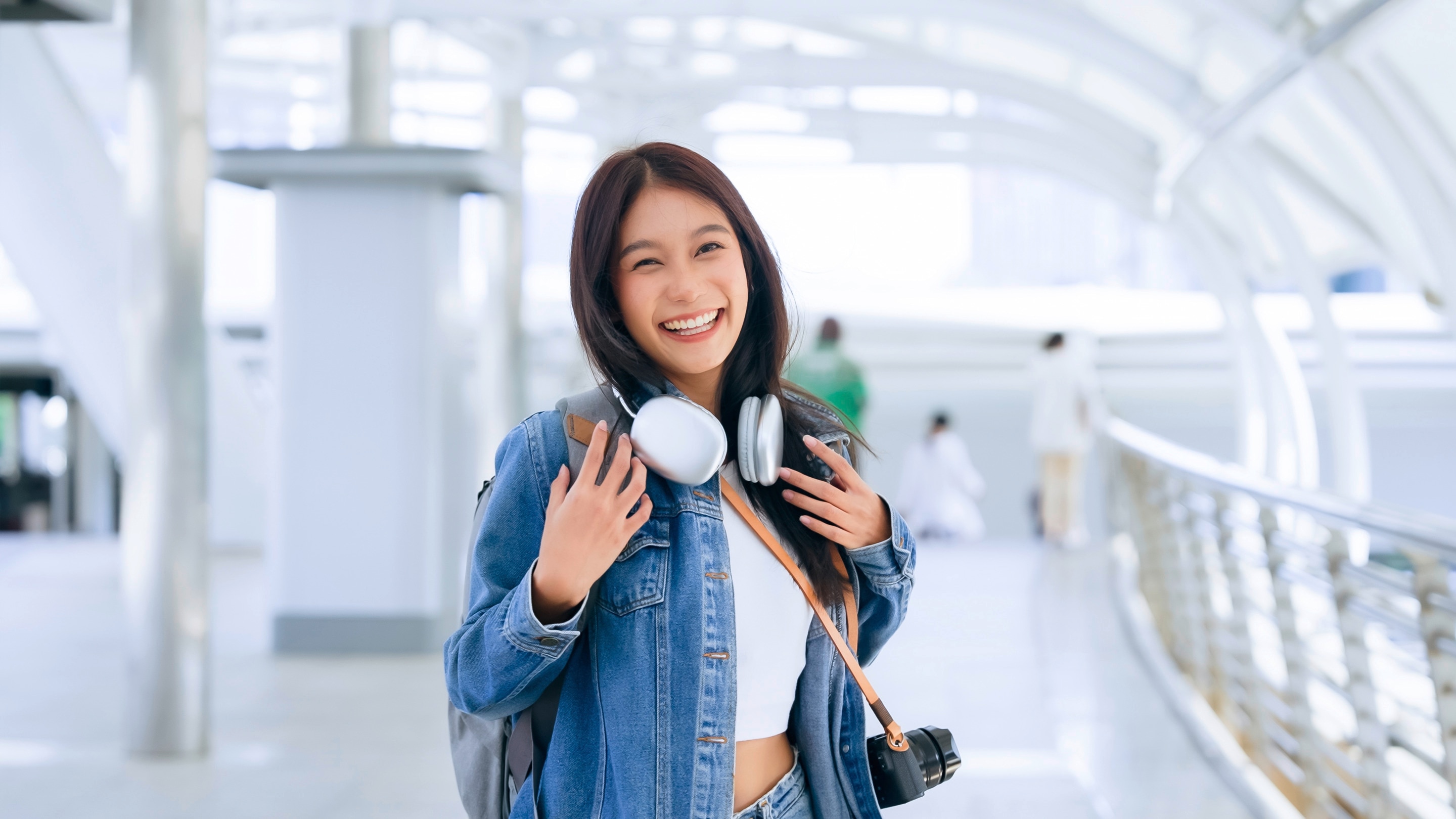 Smiling woman carrying carry-on luggage at an airport.