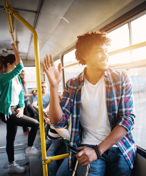 Young man on a bus waving to someone and feeling confident and wearing an effective deodorant for hyperhidrosis
