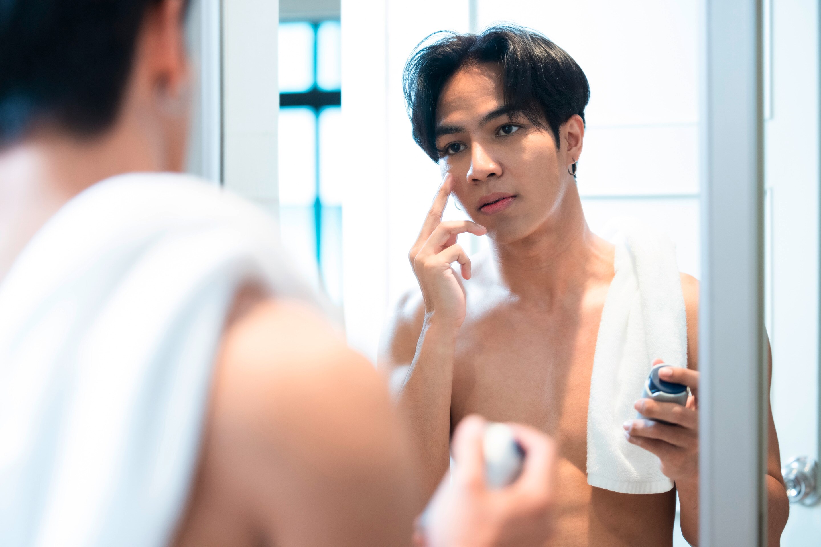 Man applying moisturizer onto his face while standing in front of a mirror.