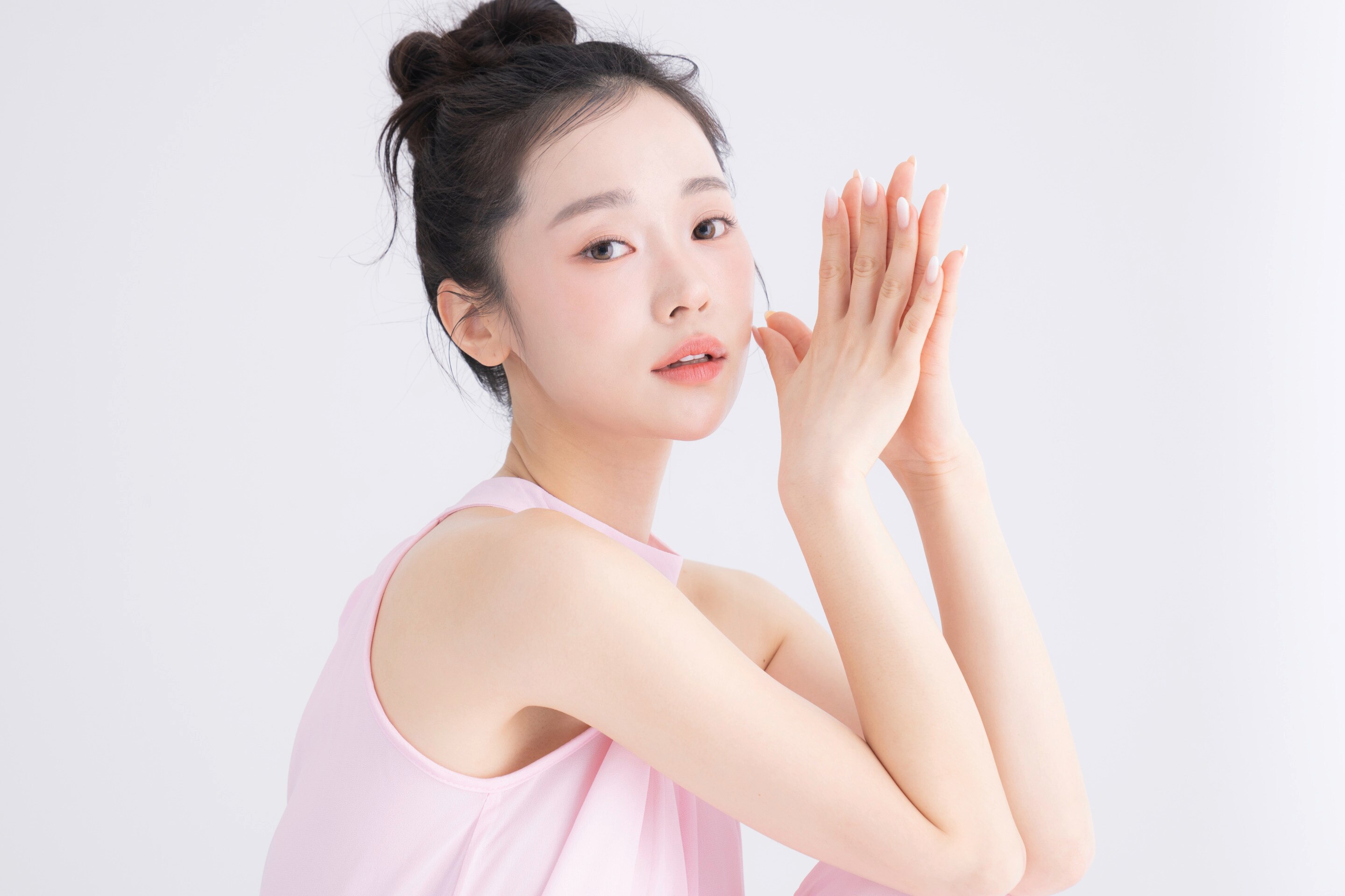 ผู้หญิงเอเชีย ผิวสวย หันข้าง หน้าเอียง เกล้าผมมวยสูง สองมือประกบยกขึ้นใกล้หน้า สวมเสื้อแขนกุดสีชมพู