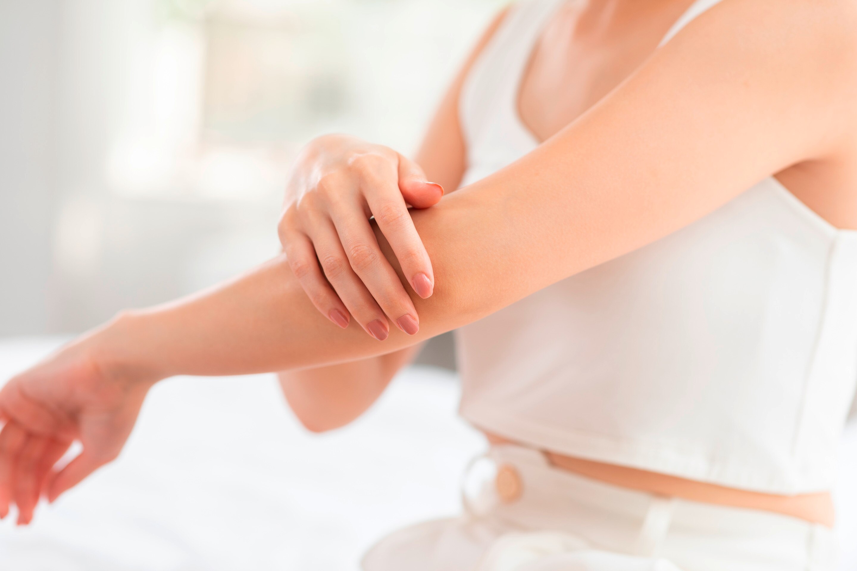 ลำตัวผู้หญิง มือข้างหนึ่งยื่นไปด้านหน้า อีกมือจับข้อศอกของมืออีกข้าง ใส่เสื้อแขนกุดสีขาว