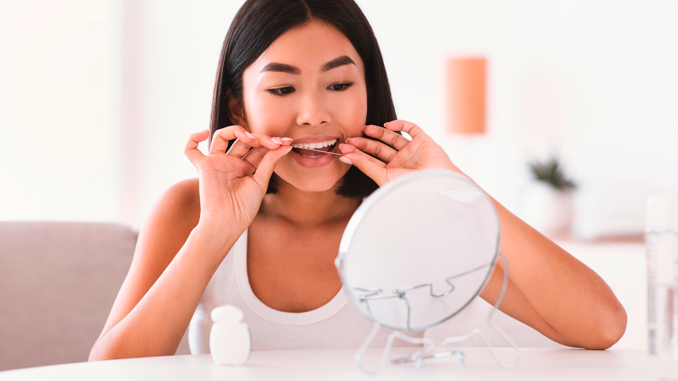 A woman flossing her teeth in front of a small mirror.