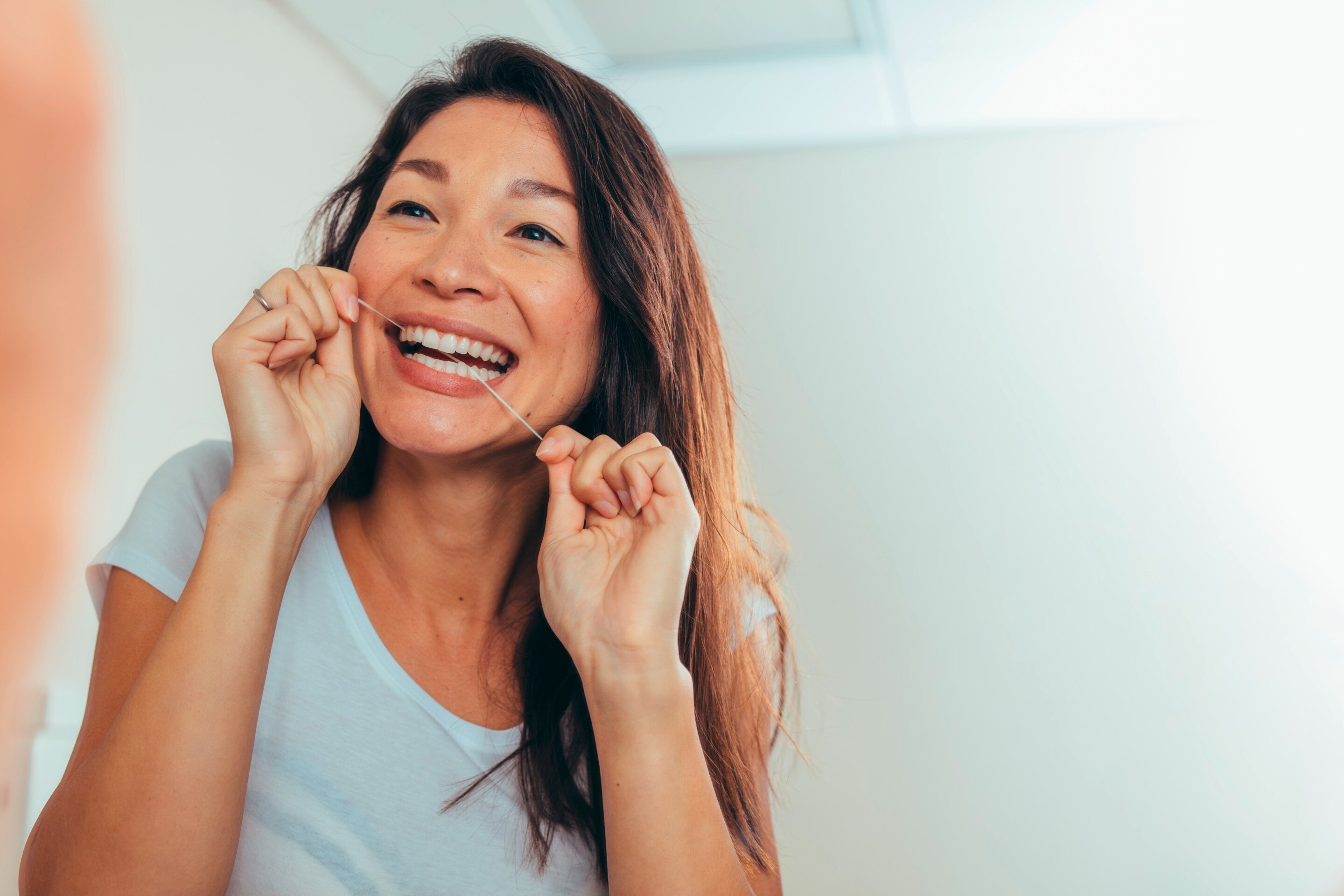 A woman with long hair flossing her teeth in front of the mirror.