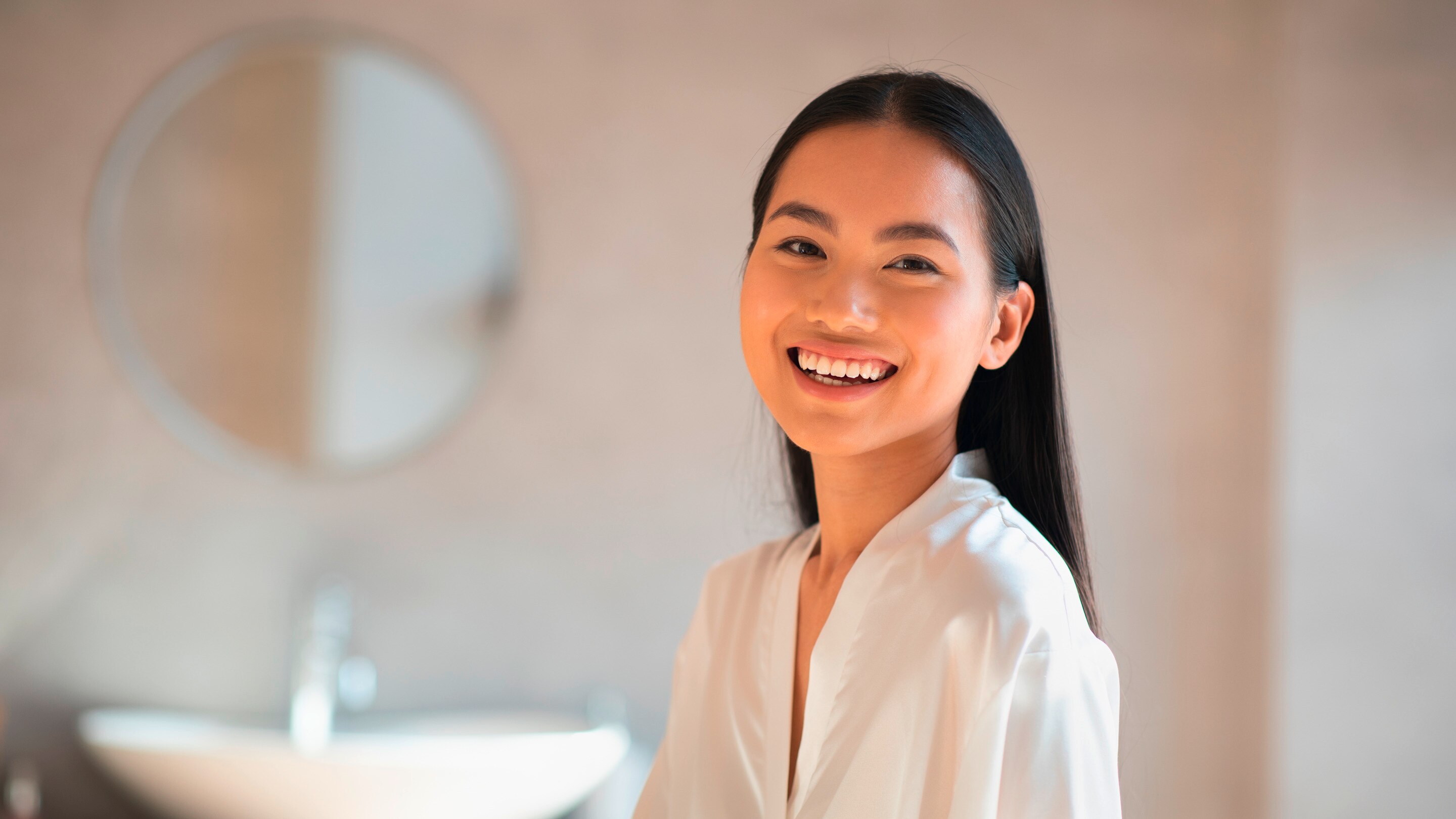 A woman with long hair smiling in the bathroom.