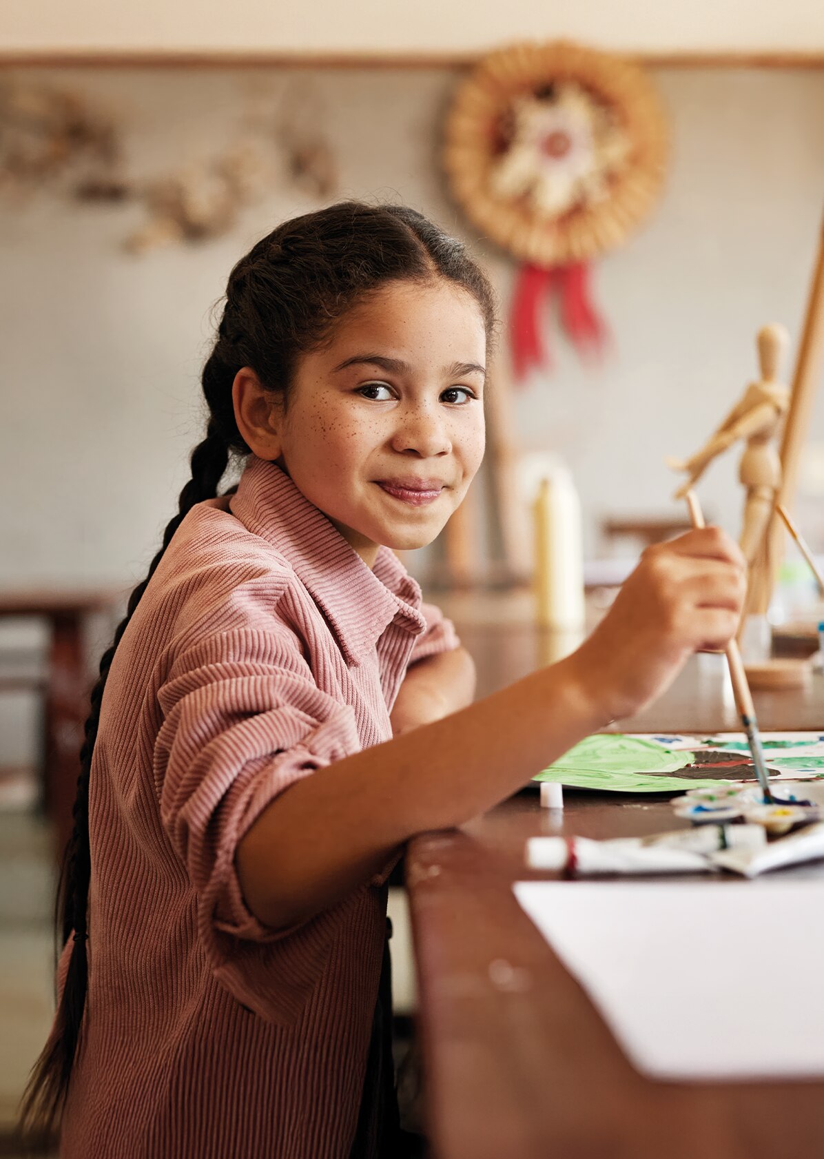 Girl smiling at a art desk holding a paint brush