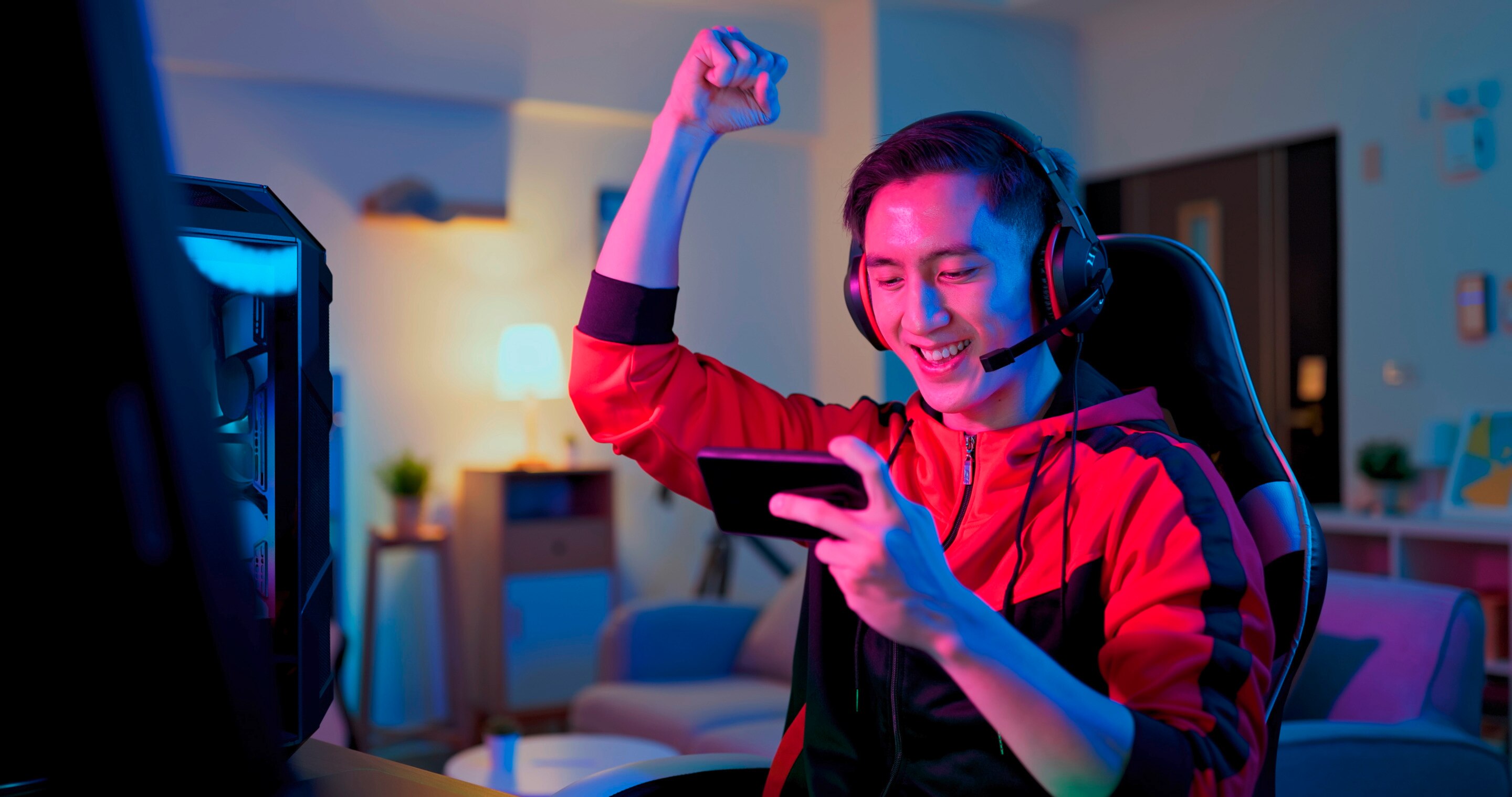 A gamer holds his phone in one hand and raises a victorious fist in the air.