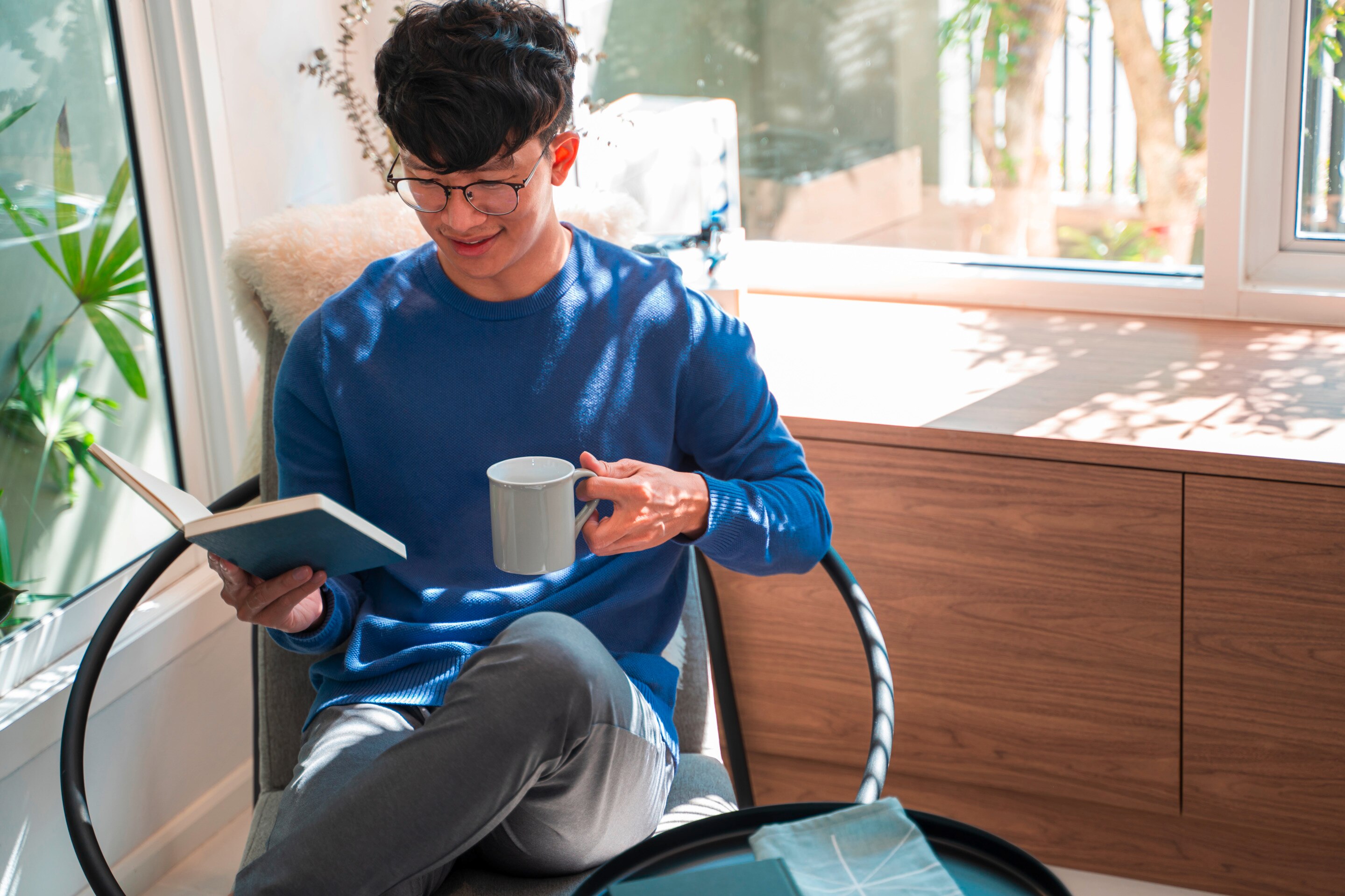 A man relaxes with a book in one hand and a mug in the other.
