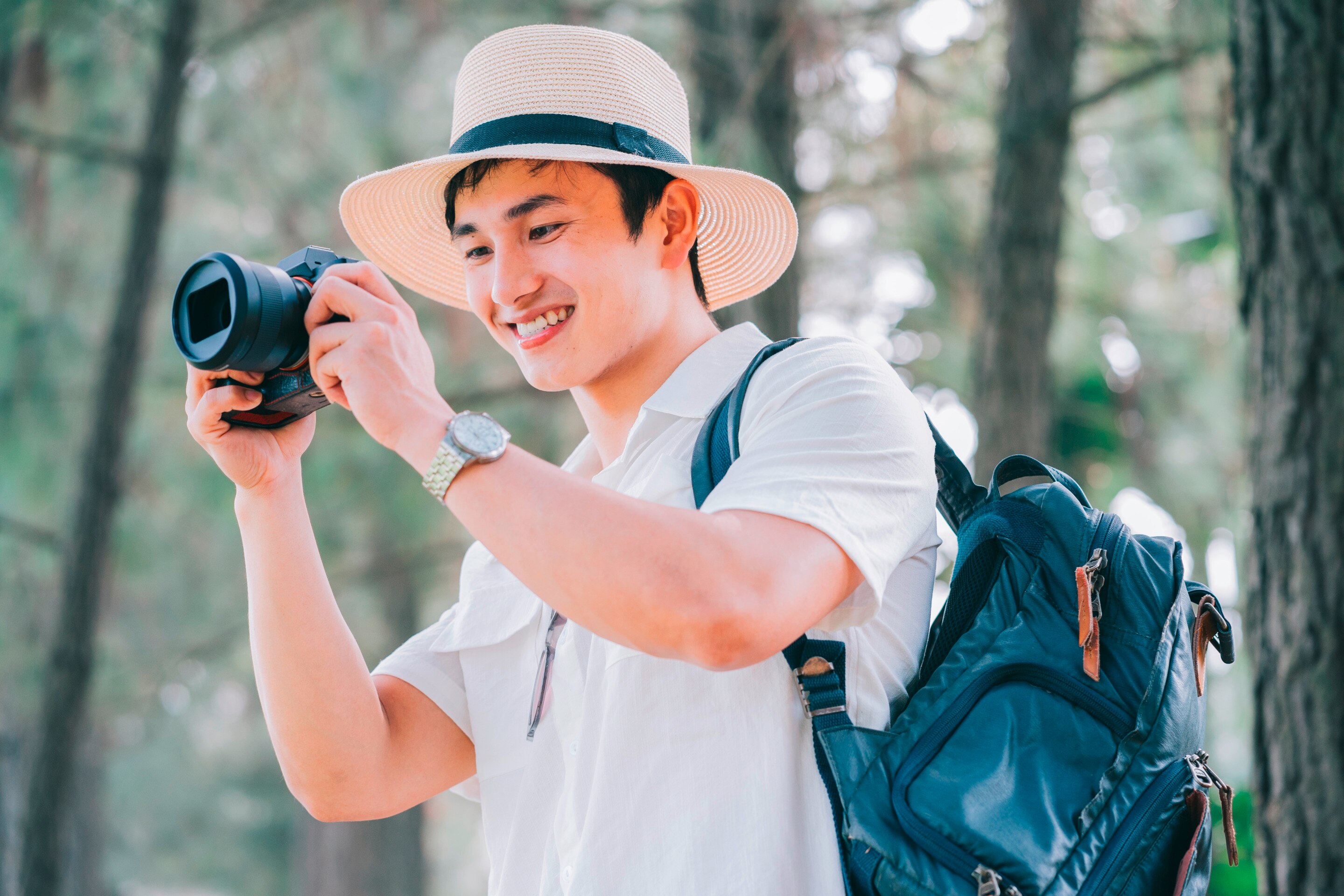 A young man with a backpack holds a camera outdoors.