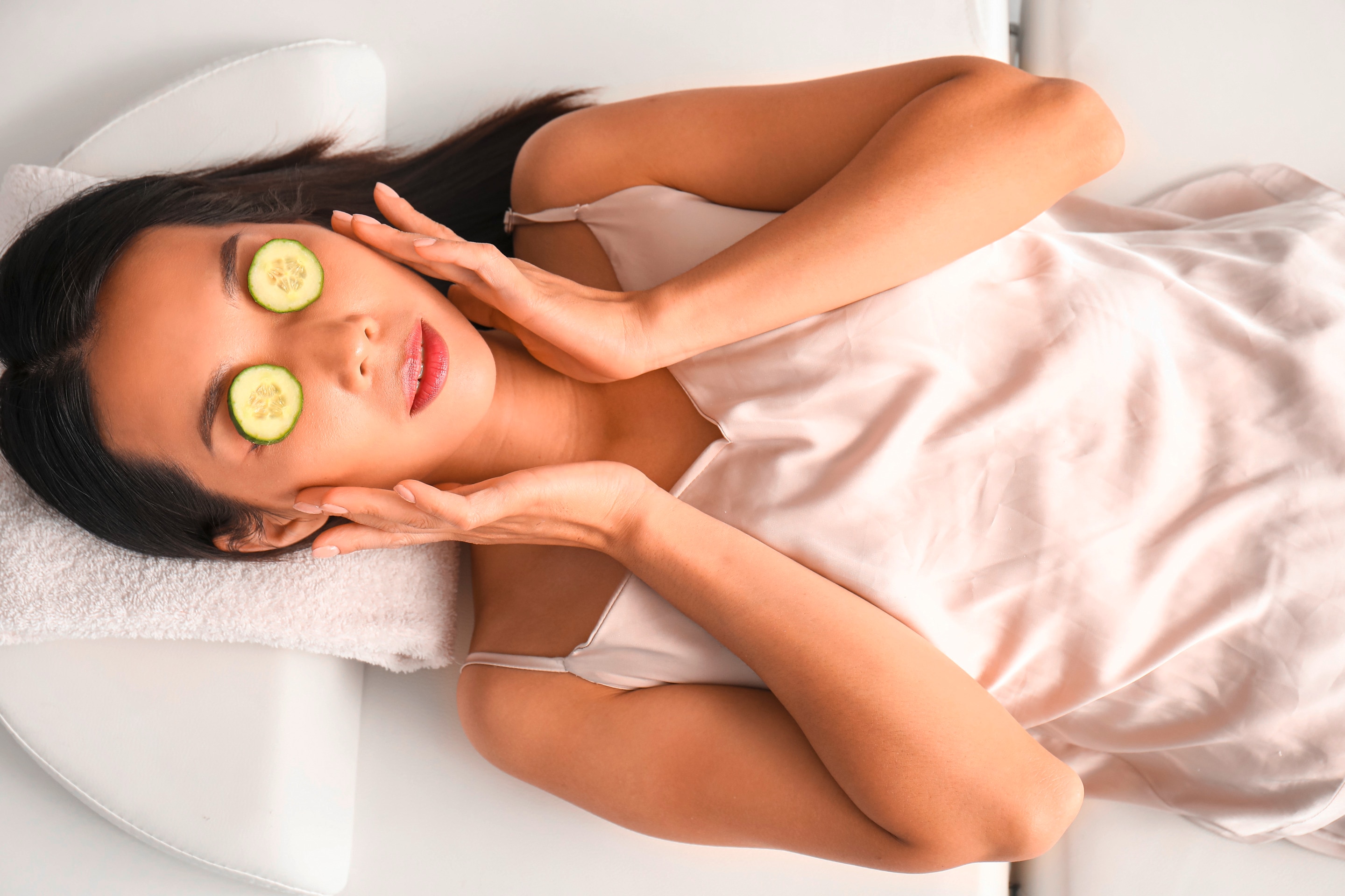Woman with cucumber slices covering her eyes relaxing on a bed.