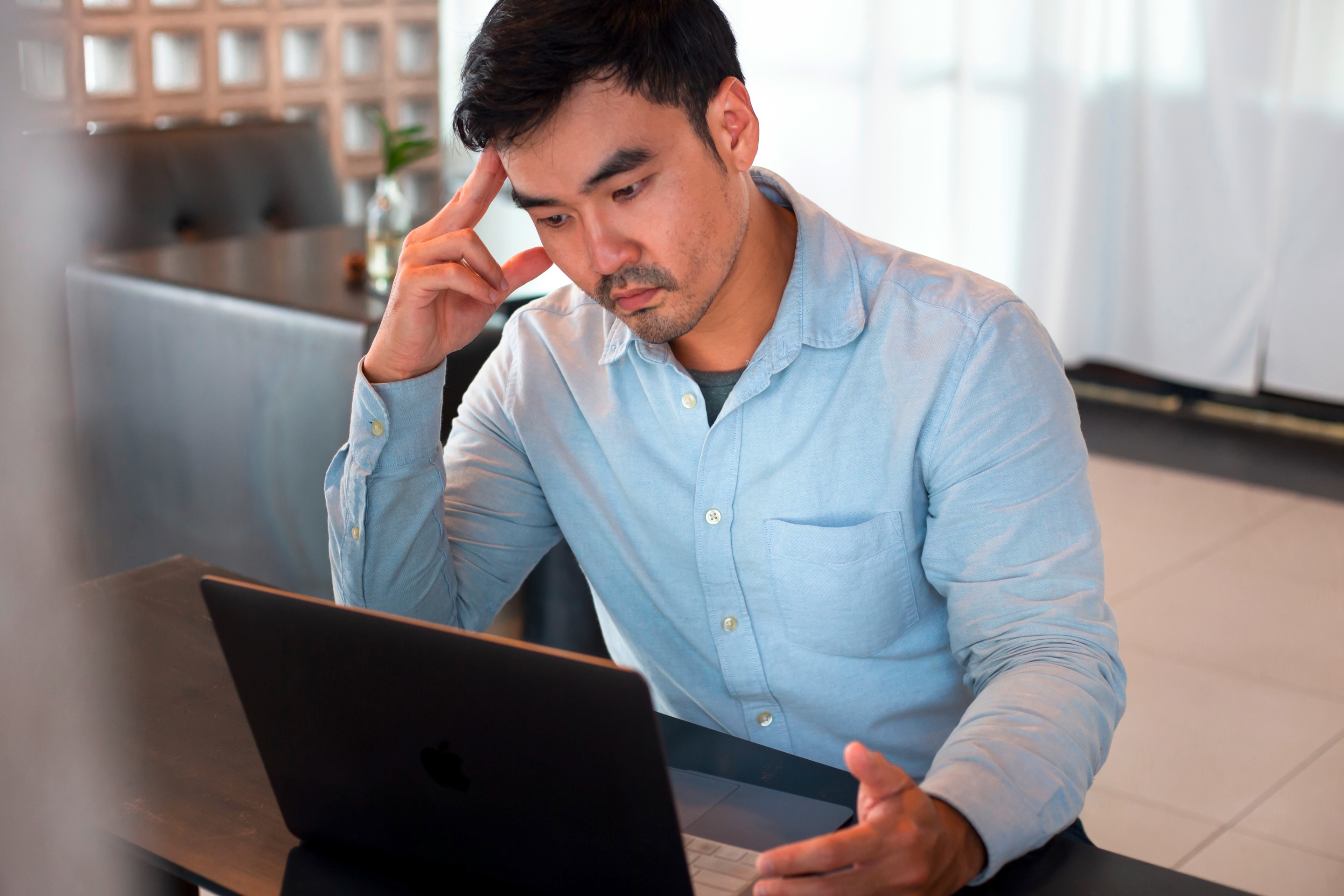 Man touching his temple while working on his laptop.