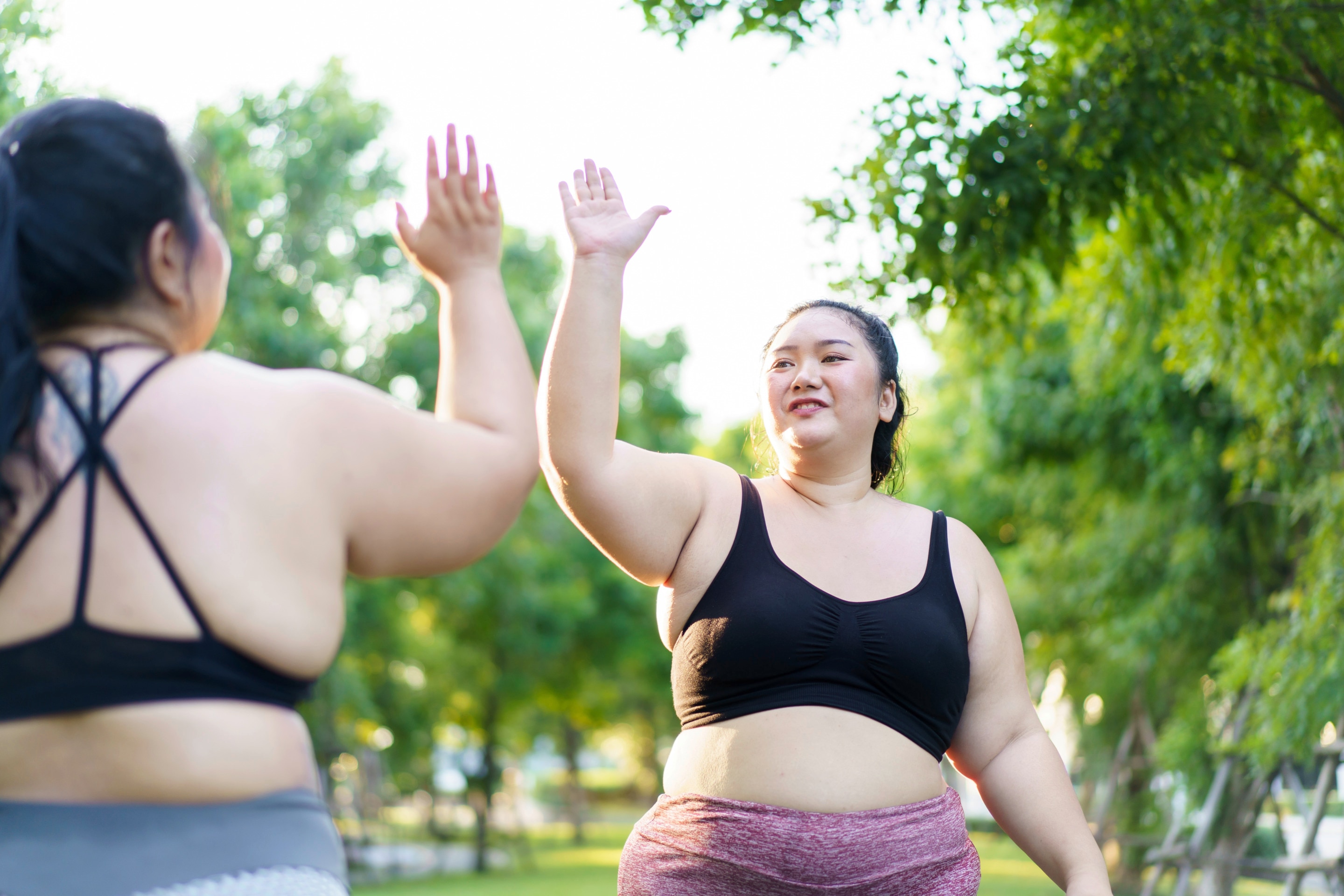 Two women in workout gear high-fiving each other at a park.