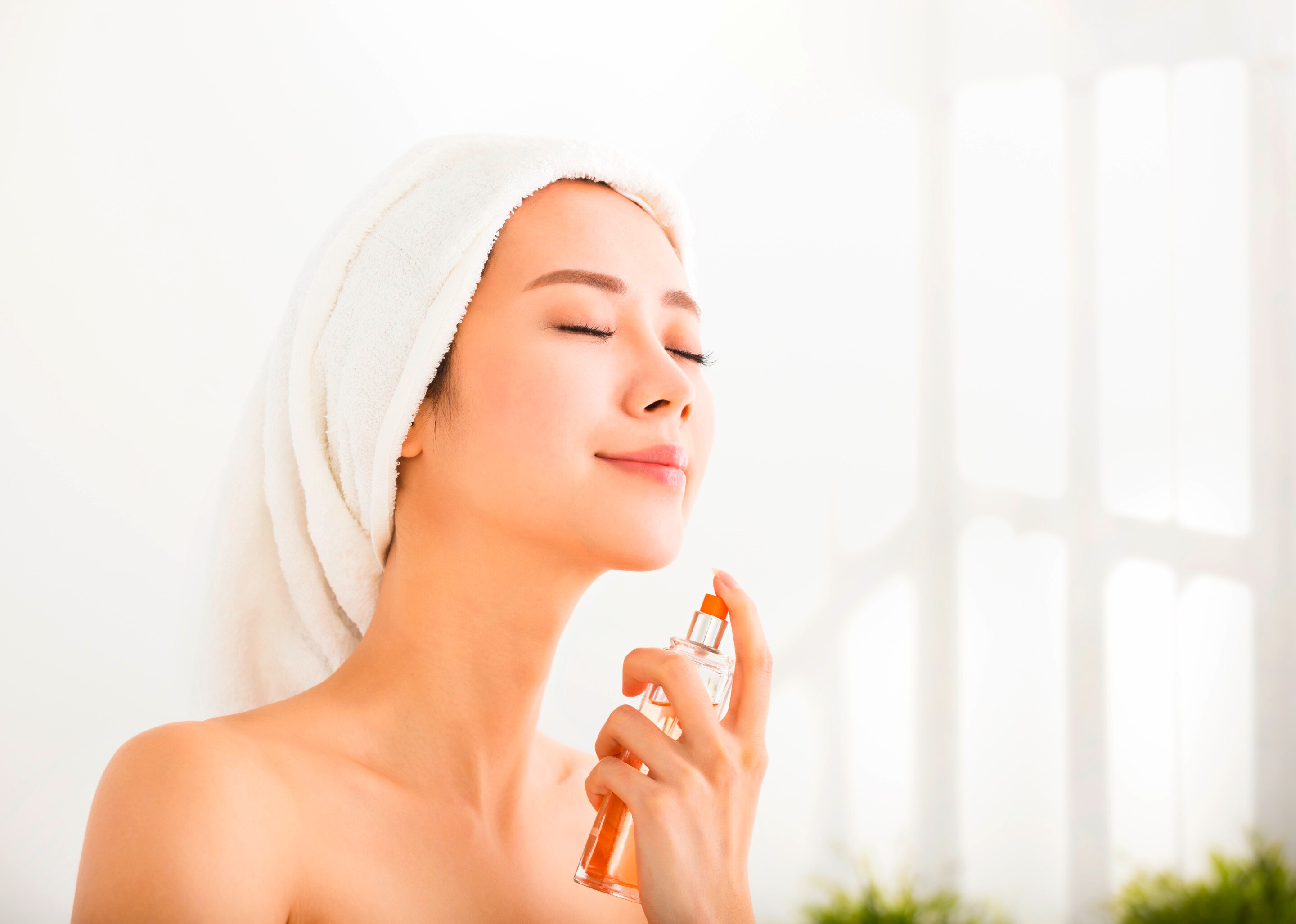 Woman with a towel on her head spraying perfume.