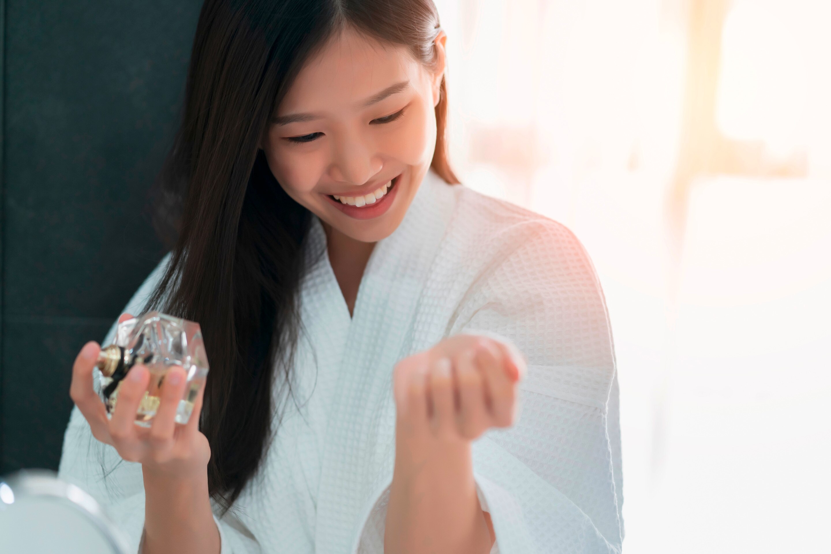 Smiling woman in bathrobe applying perfume on her wrist.