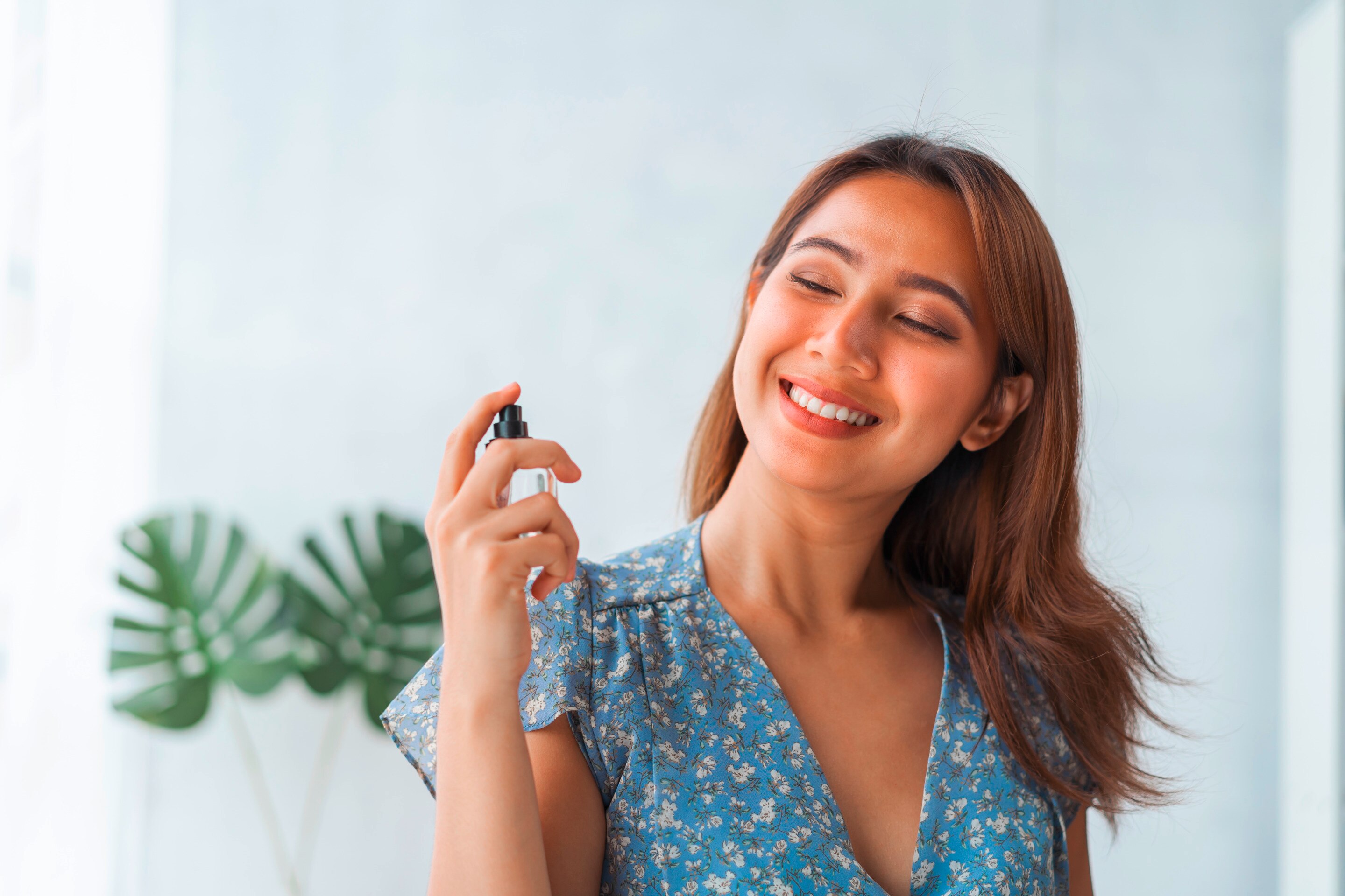 Smiling woman spraying perfume on her neck.