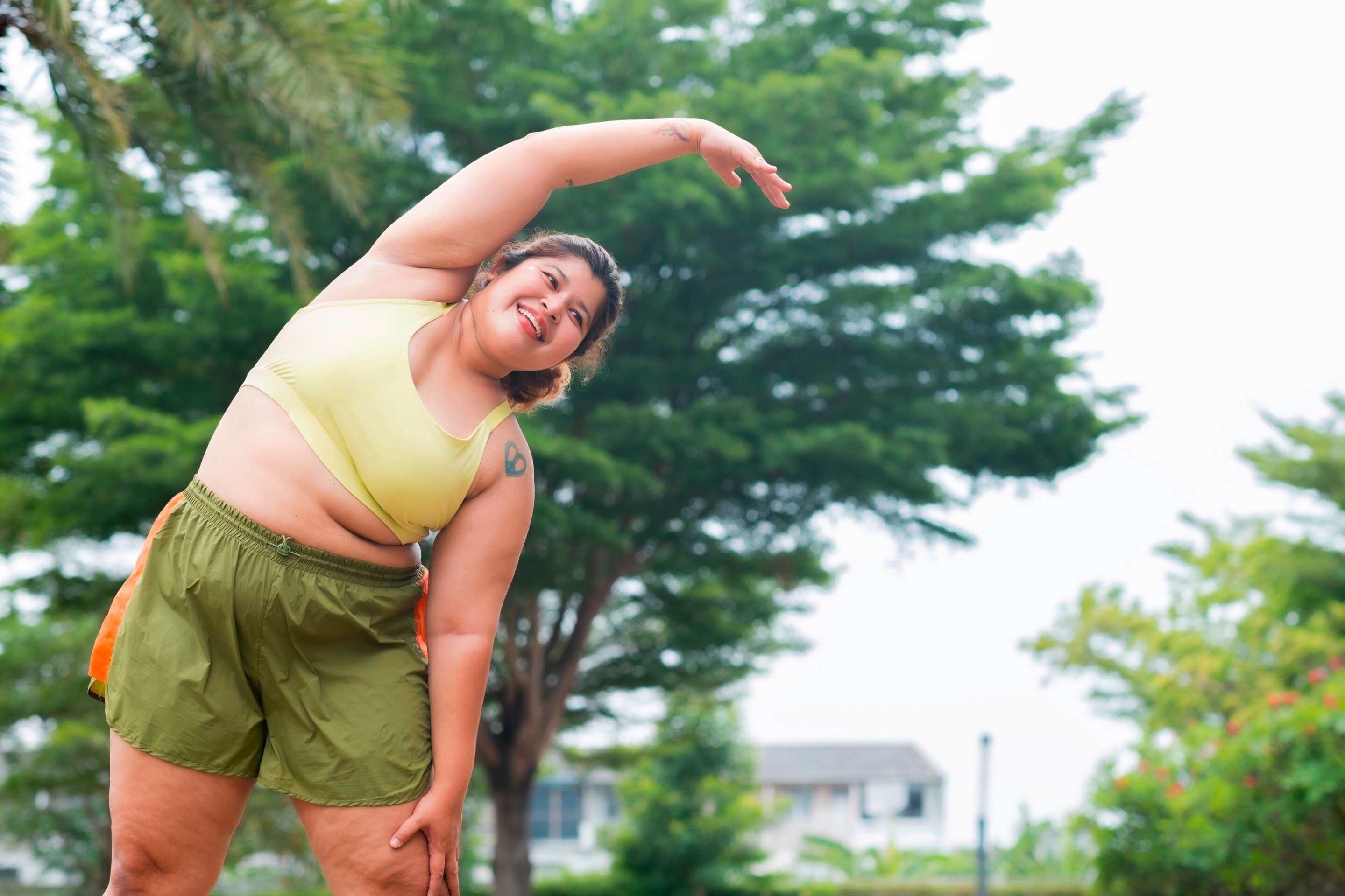 Woman in sports bra and shorts stretching her body outdoors.
