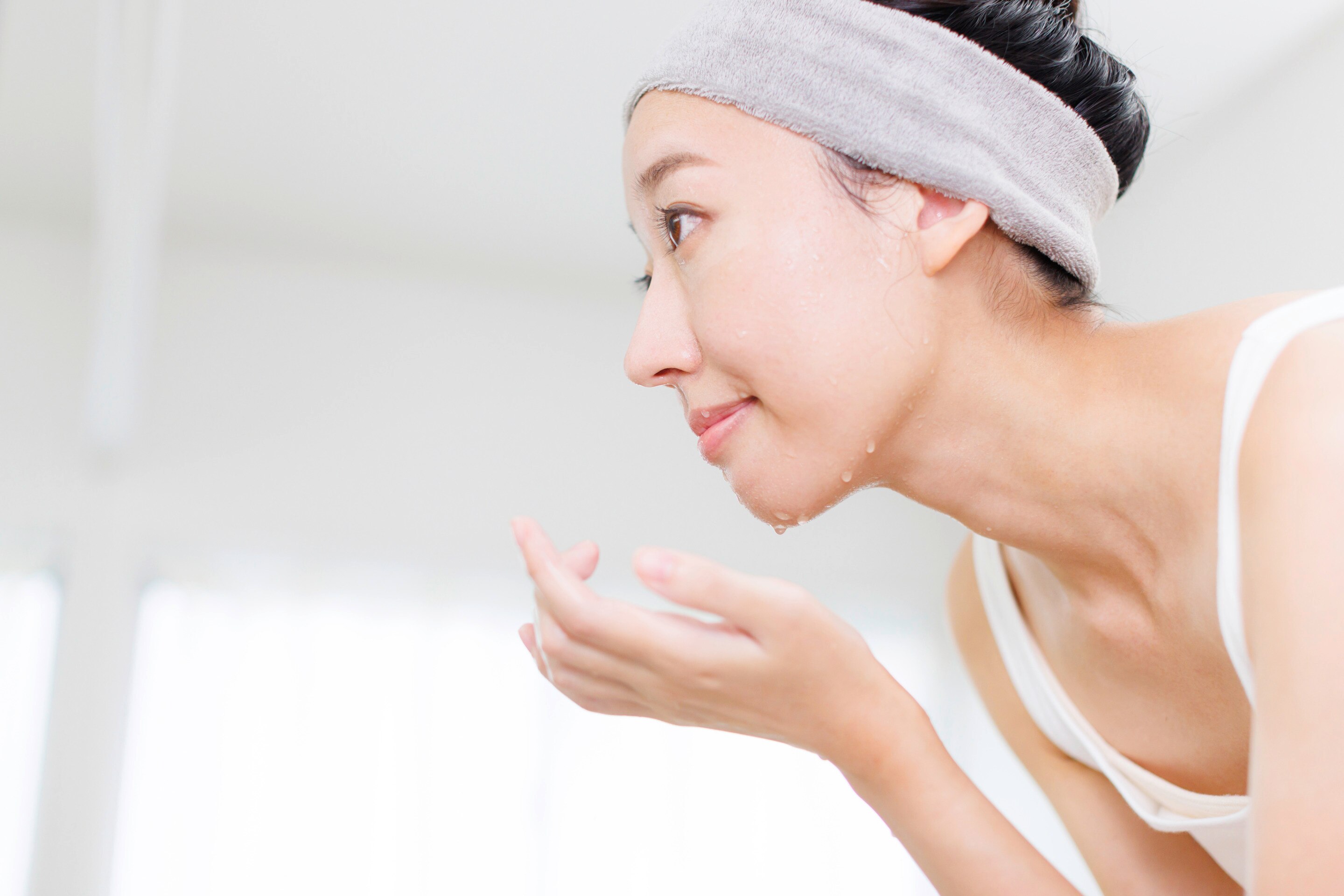 Woman with headband washing her face in a bathroom.
