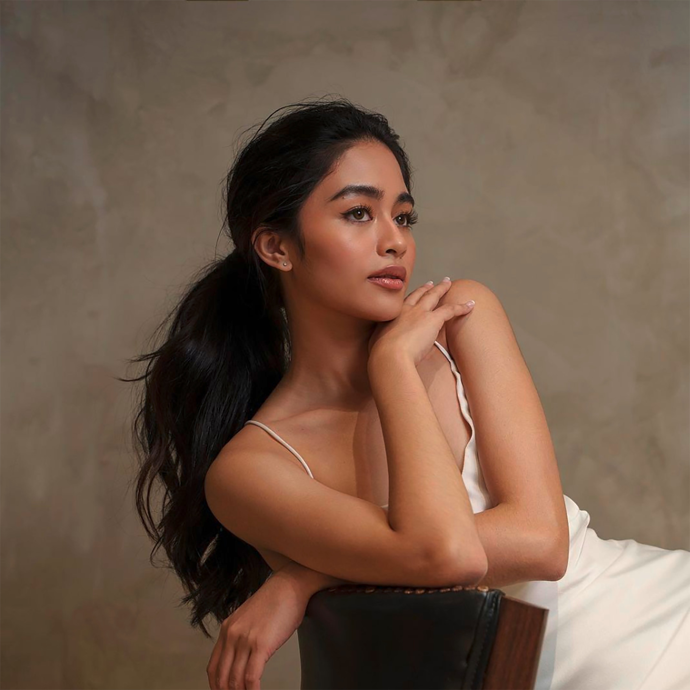 A Filipina actress with textured low ponytail sitting on a chair.