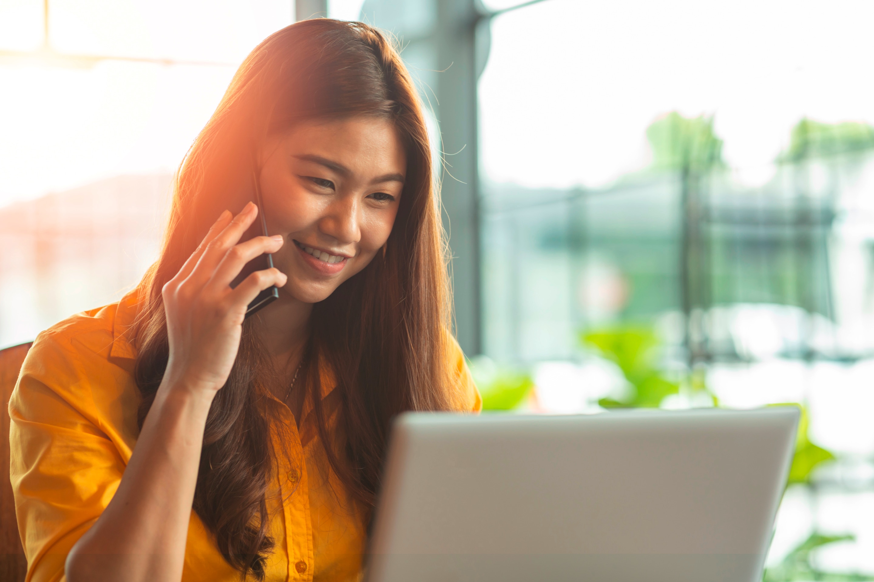 Happy Asian woman on work call in sunny room.