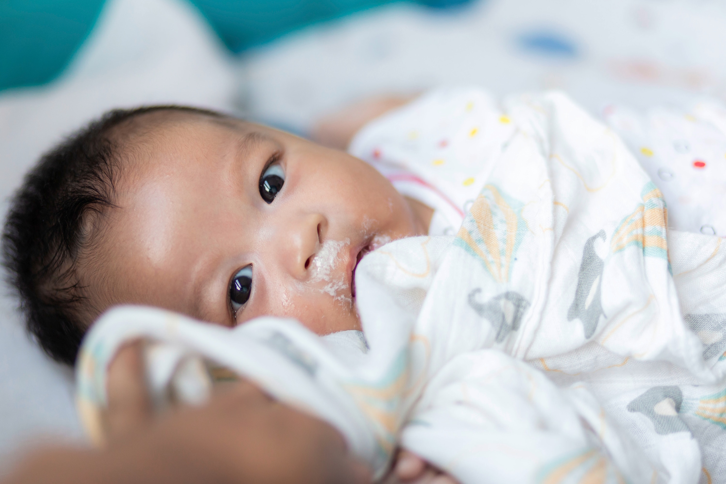 bayi berbaring sambil dibedong, dengan sisa susu di sekitar mulut setelah menyusu karena gumoh.
