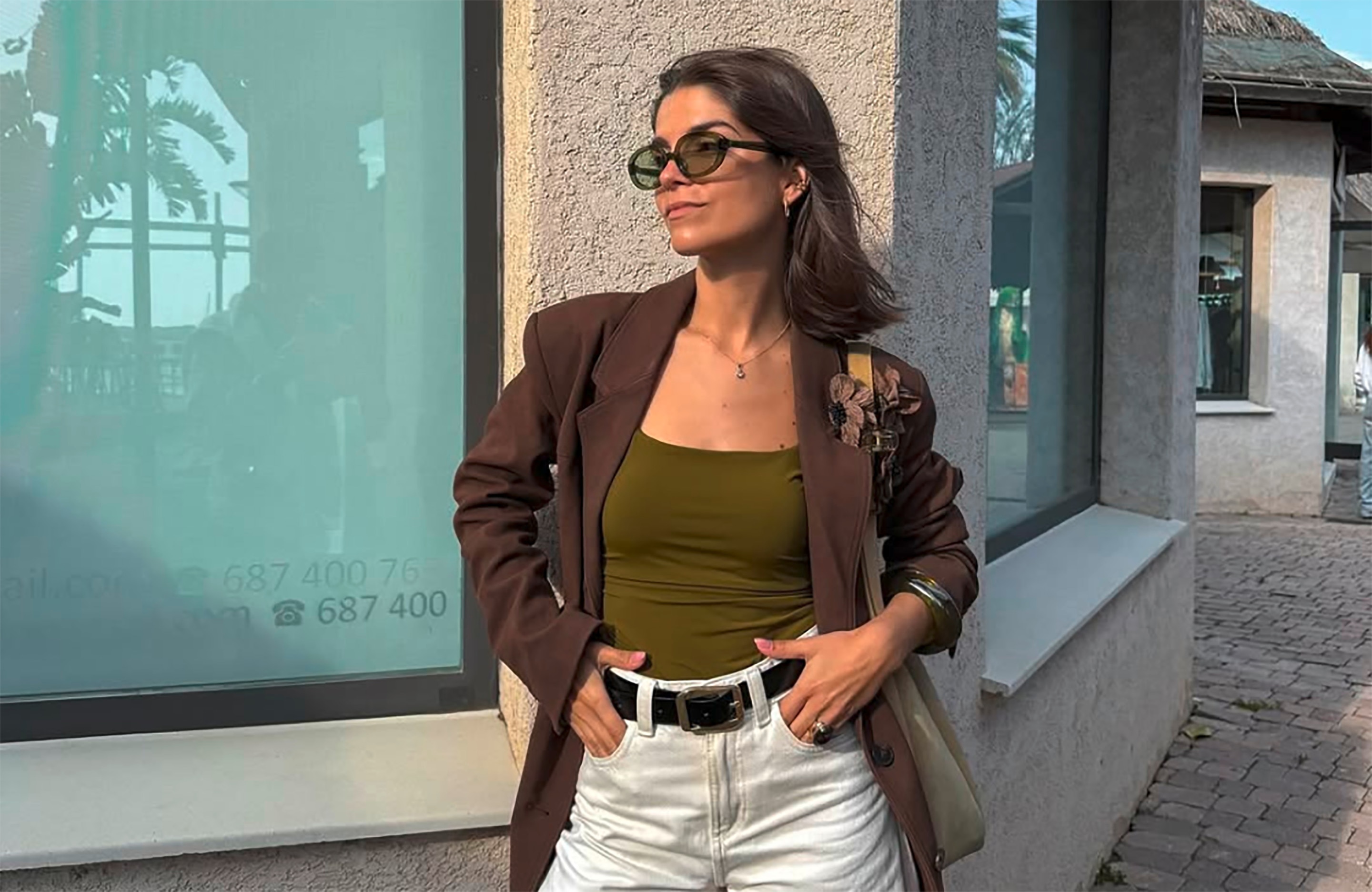 Woman wearing an olive-colored top, brown blazer with a flower brooch, and white jeans.