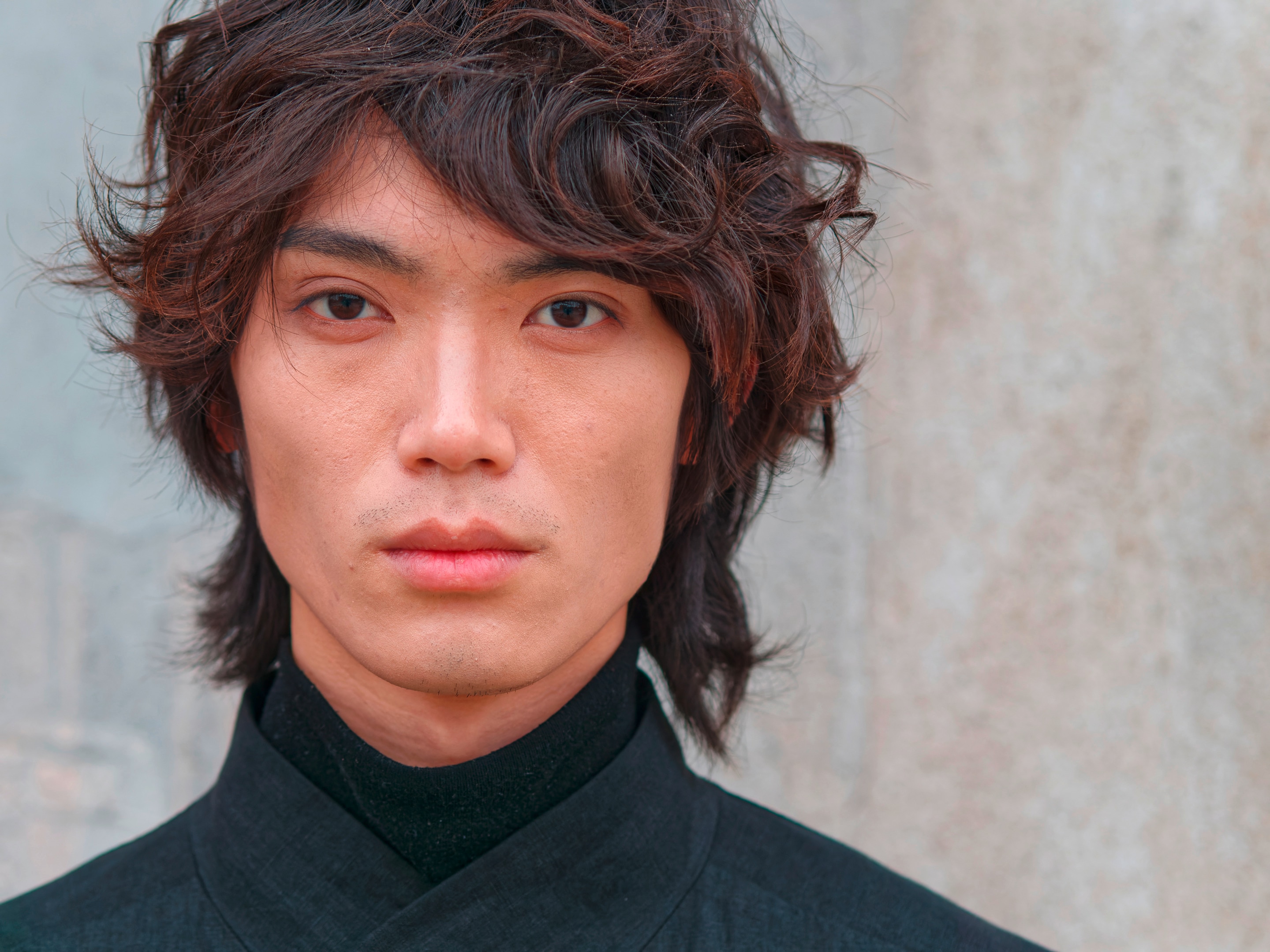 ผู้ชายเอเชีย ผมหยักศก ผมดัดลอน หน้าม้าปัดข้าง ผมทำสี ผมยาวถึงต้นคอ สวมเสื้อสีดำ