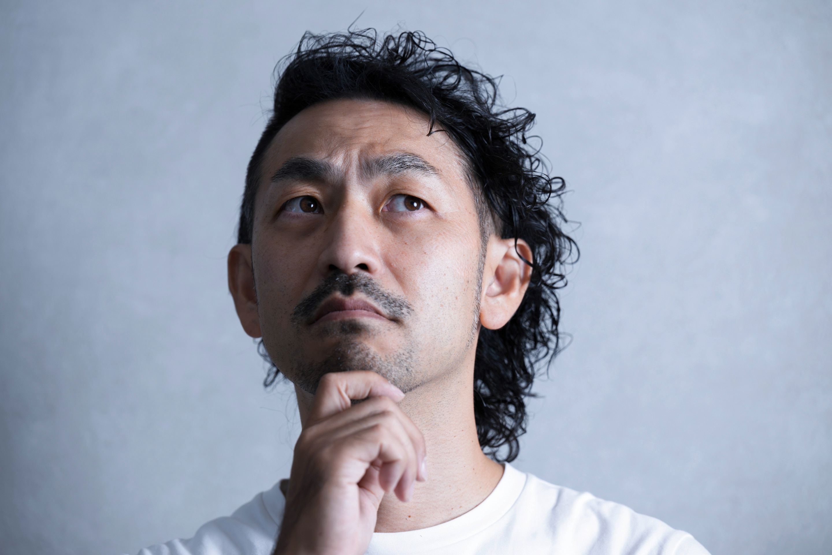 ชายเอเชีย ผมหยิก ผมหยักศก ผมดัดลอน แสกข้าง มือจับที่คาง สวมเสื้อยืดสีขาว