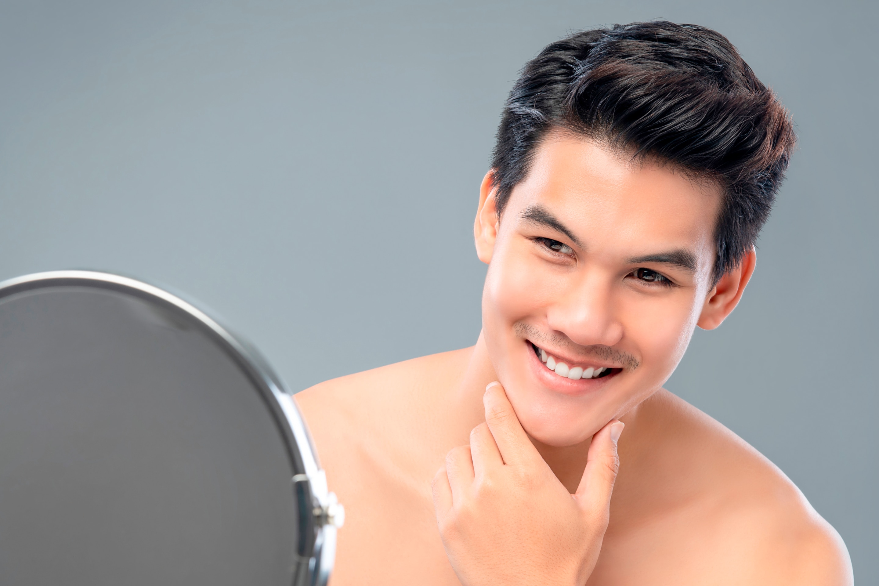 Gen Z dengan rambut rapi sedang tersenyum sambil melihat ke cermin, memeriksa wajahnya sebagai bagian dari personal grooming