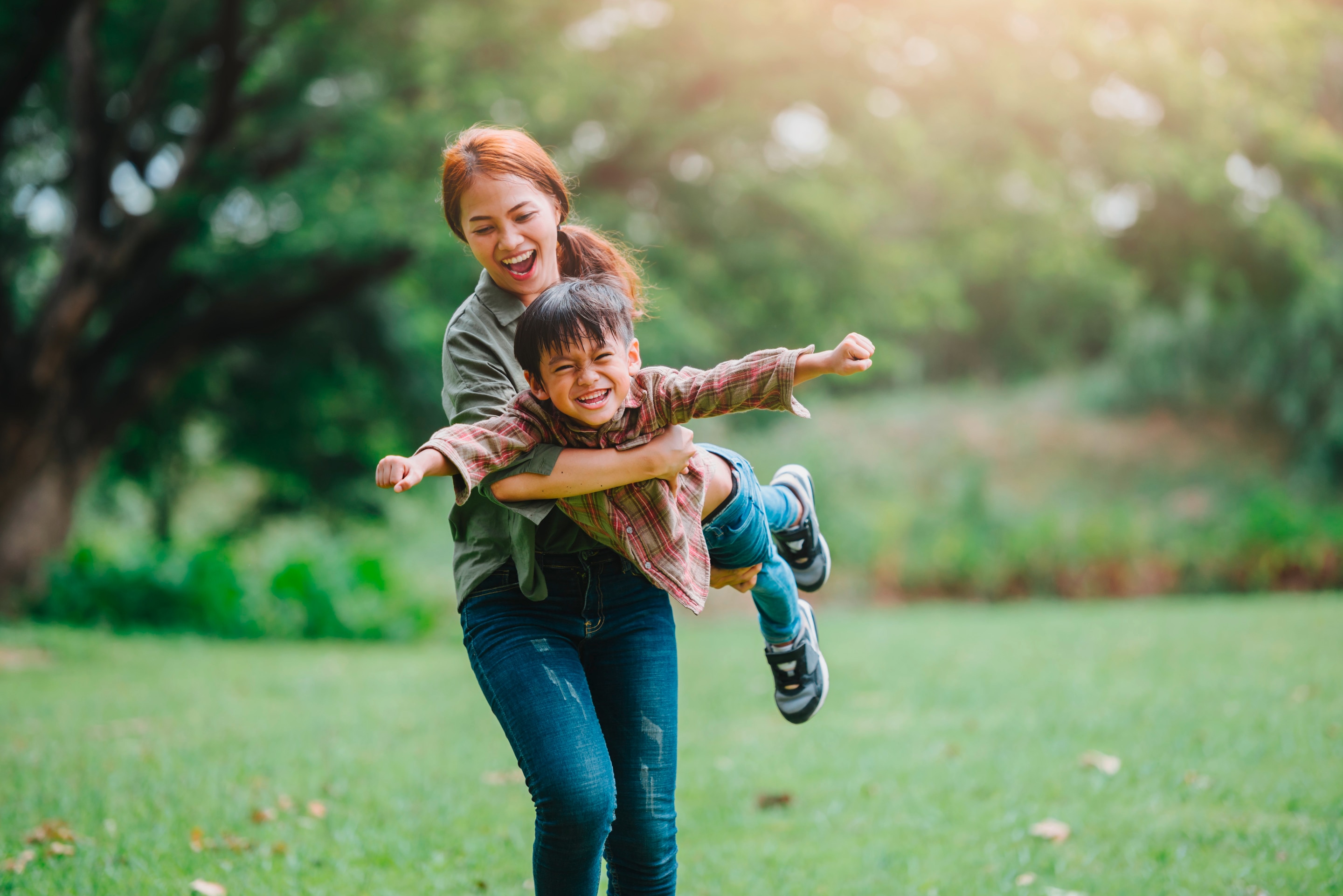 Young smiling Asian mom playing airplane with young son.