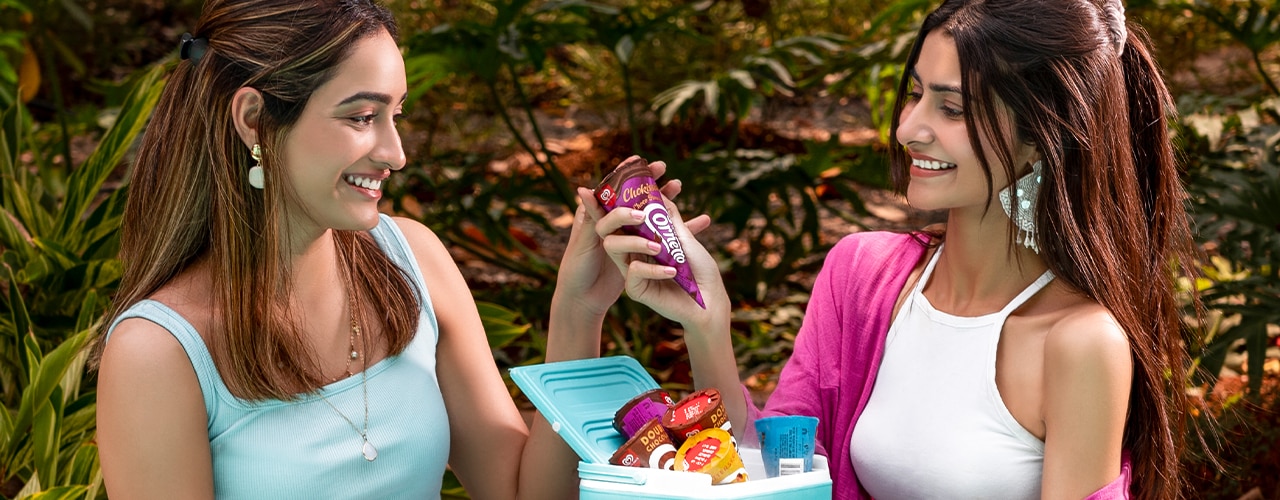 Two young people halding Twister ice creams amid water splashes against bright blue sky.