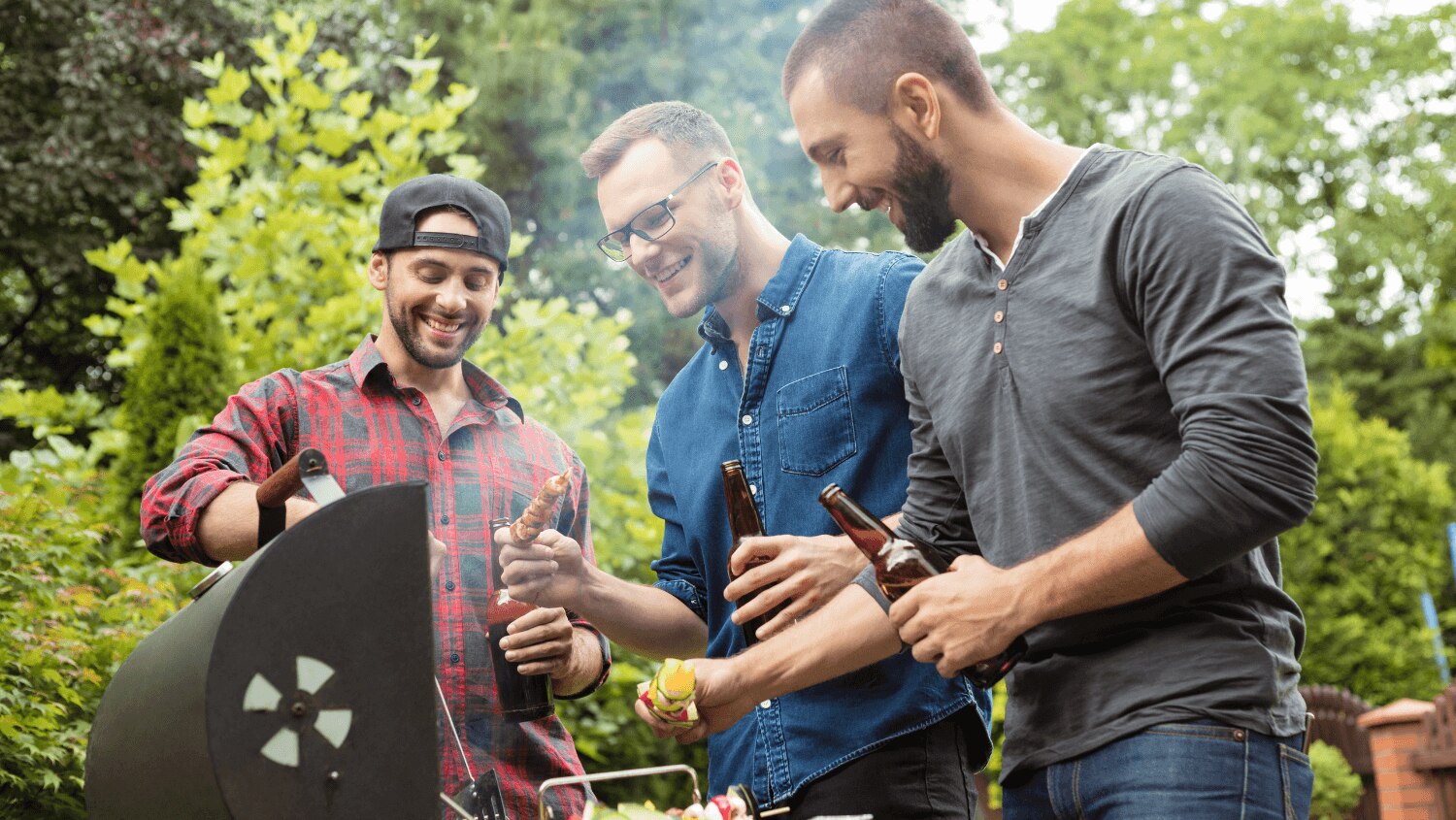 Three male friends barbequing together with charcoal 