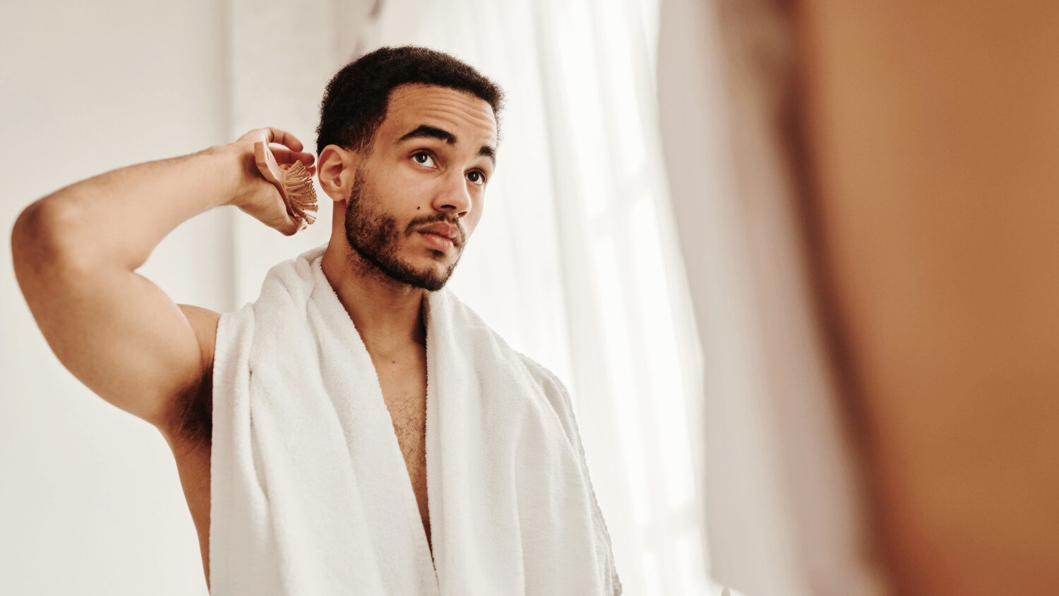 Young African American male brushing his hair in the bathroom mirror after using sulfate shampoo