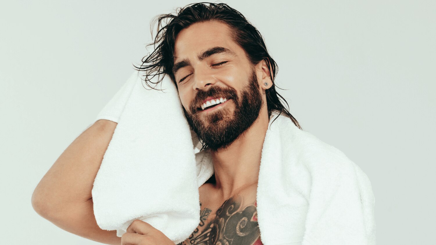 Young tattooed male towel drying his hair after washing it with sodium laureth sulfate shampoo. 