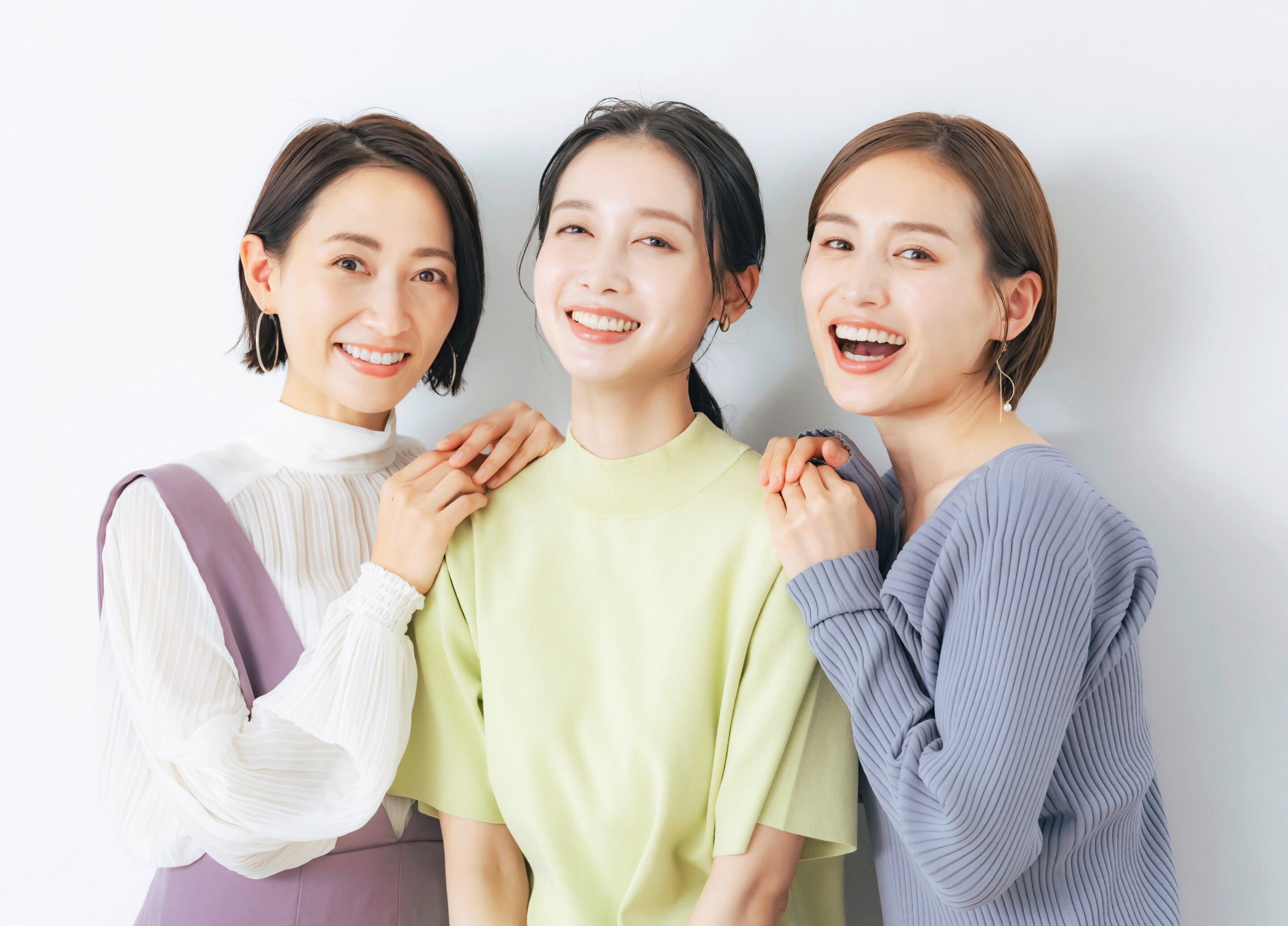 ผู้หญิงเอเชีย สามคนสามวัย ใบหน้ายิ้มเห็นฟัน ผิวสวย สองคนด้านข้างเอามือกุมหัวไหล่คนตรงกลาง 