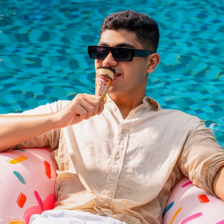 Two smiling children with curly hair holding colorful Twister ice cream against a pink background.