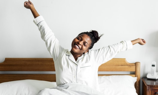 Happy black woman waking up feeling refreshed after a good nights sleep with no PCOS night sweats
