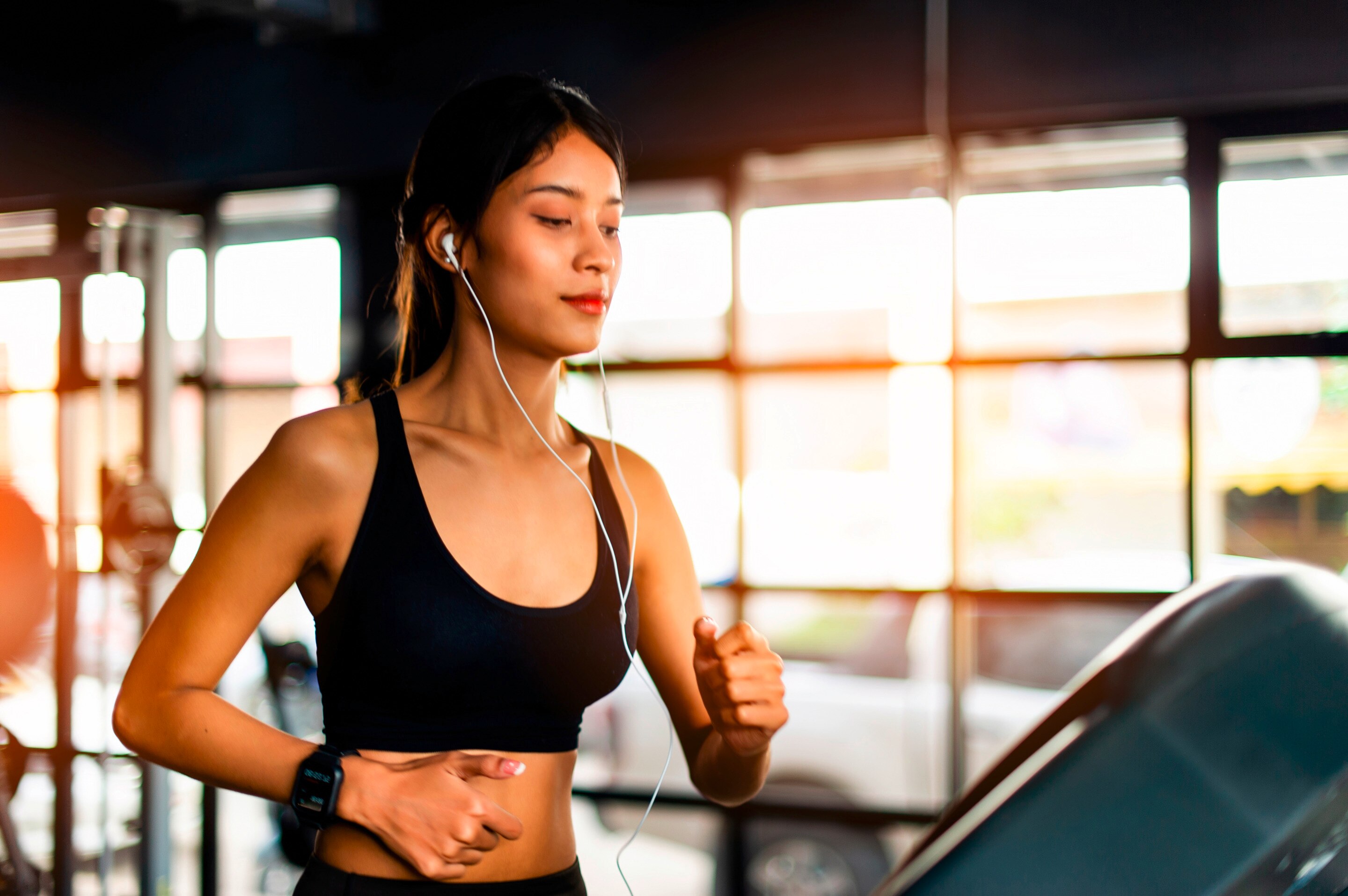 Asian woman with wired earphones running on treadmill.